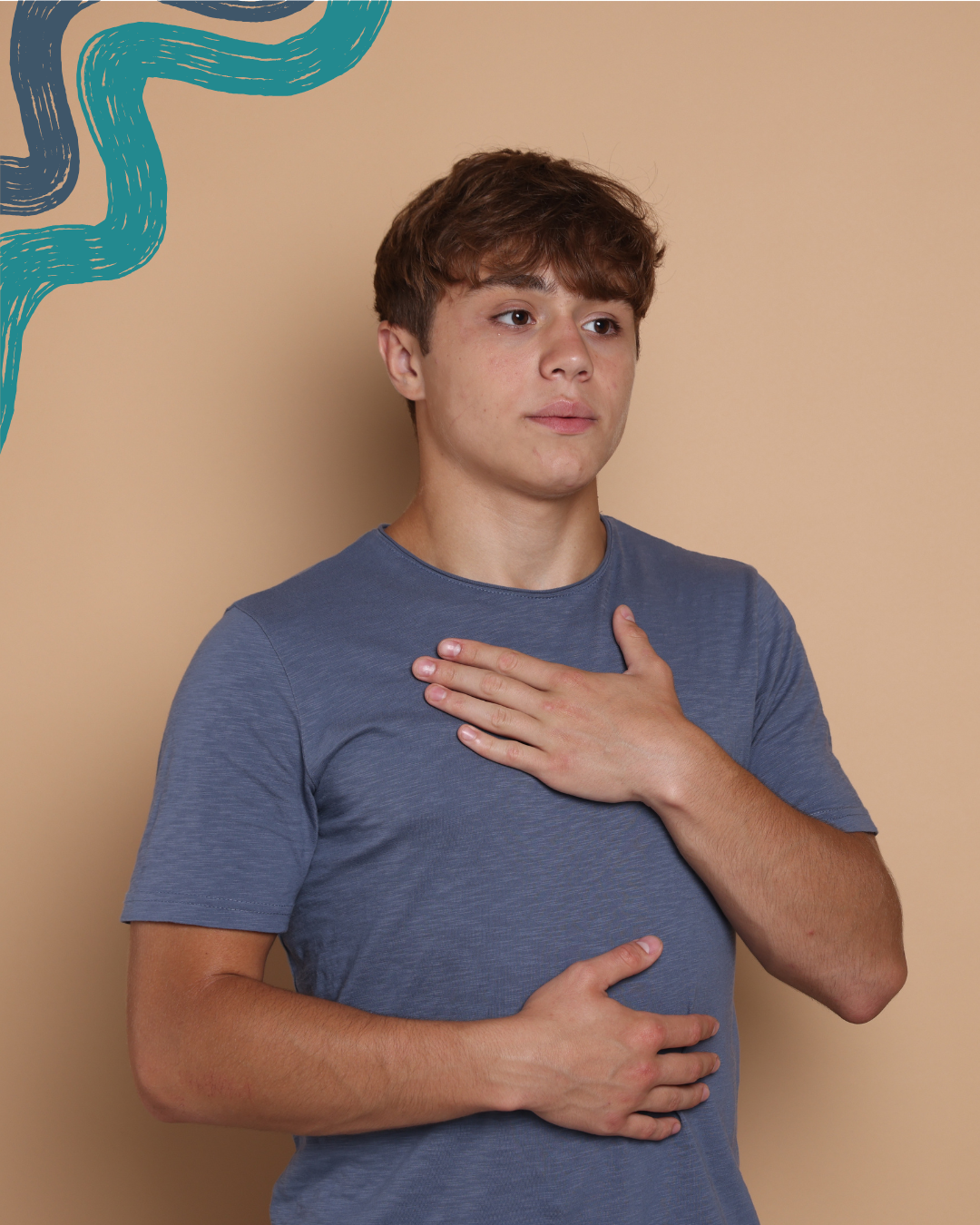 A teenage boy with brown hair and fair skin standing against a beige wall, wearing a blue t-shirt, with one hand on his chest and the other on his stomach, looking thoughtful.