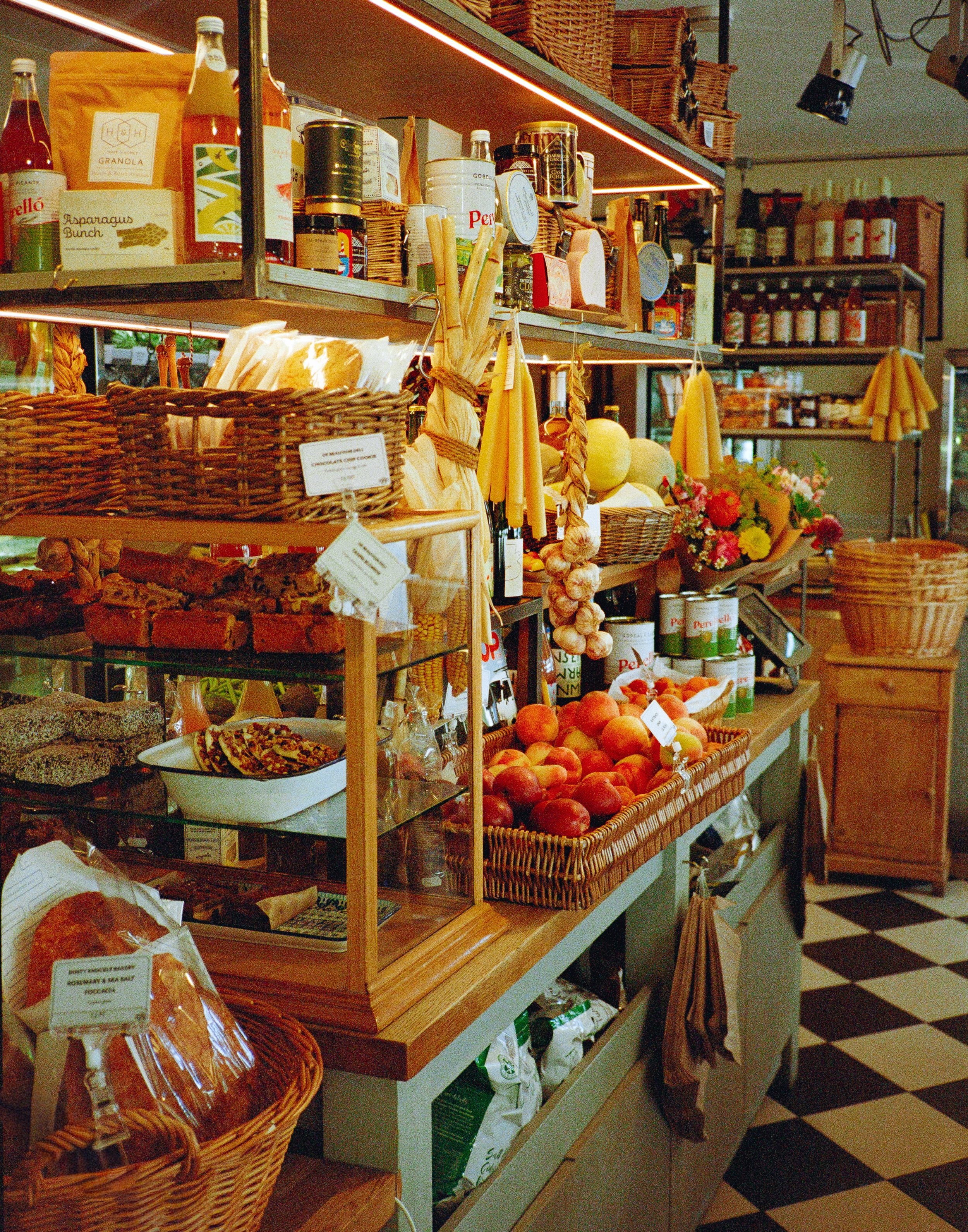 A grocery store display with apples, garlic, bread, and various canned and packaged goods on wooden shelves and baskets.