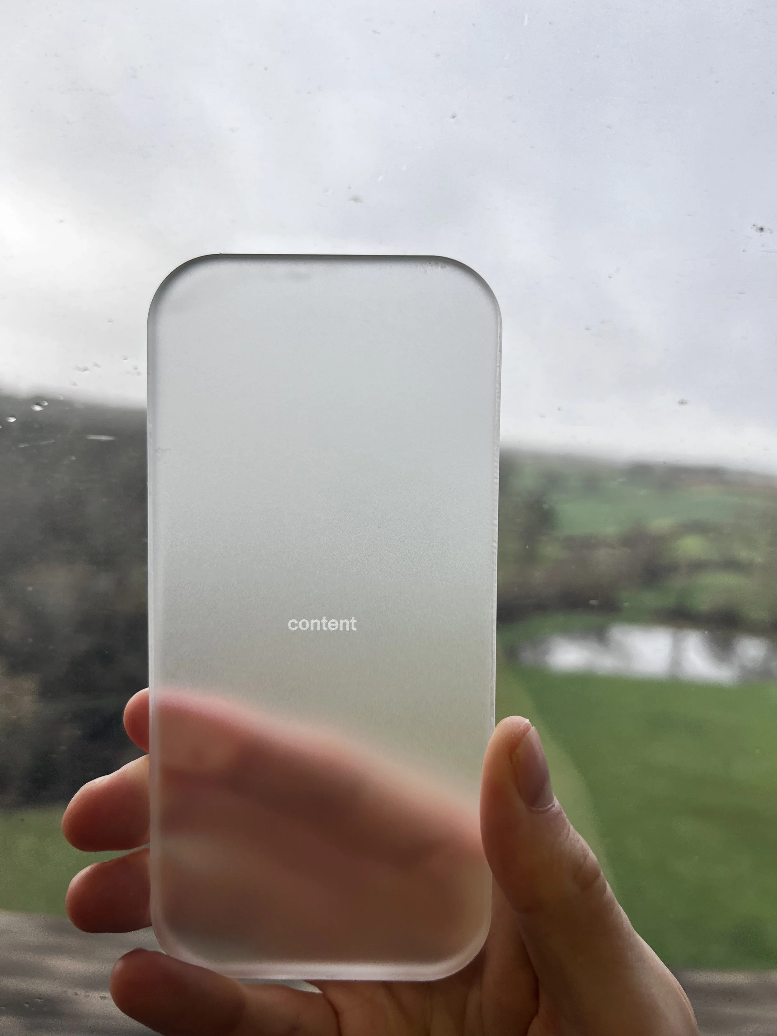 Hand holding a frosted glass bottle with the word 'content' printed on it, with a cloudy outdoor scene in the background.