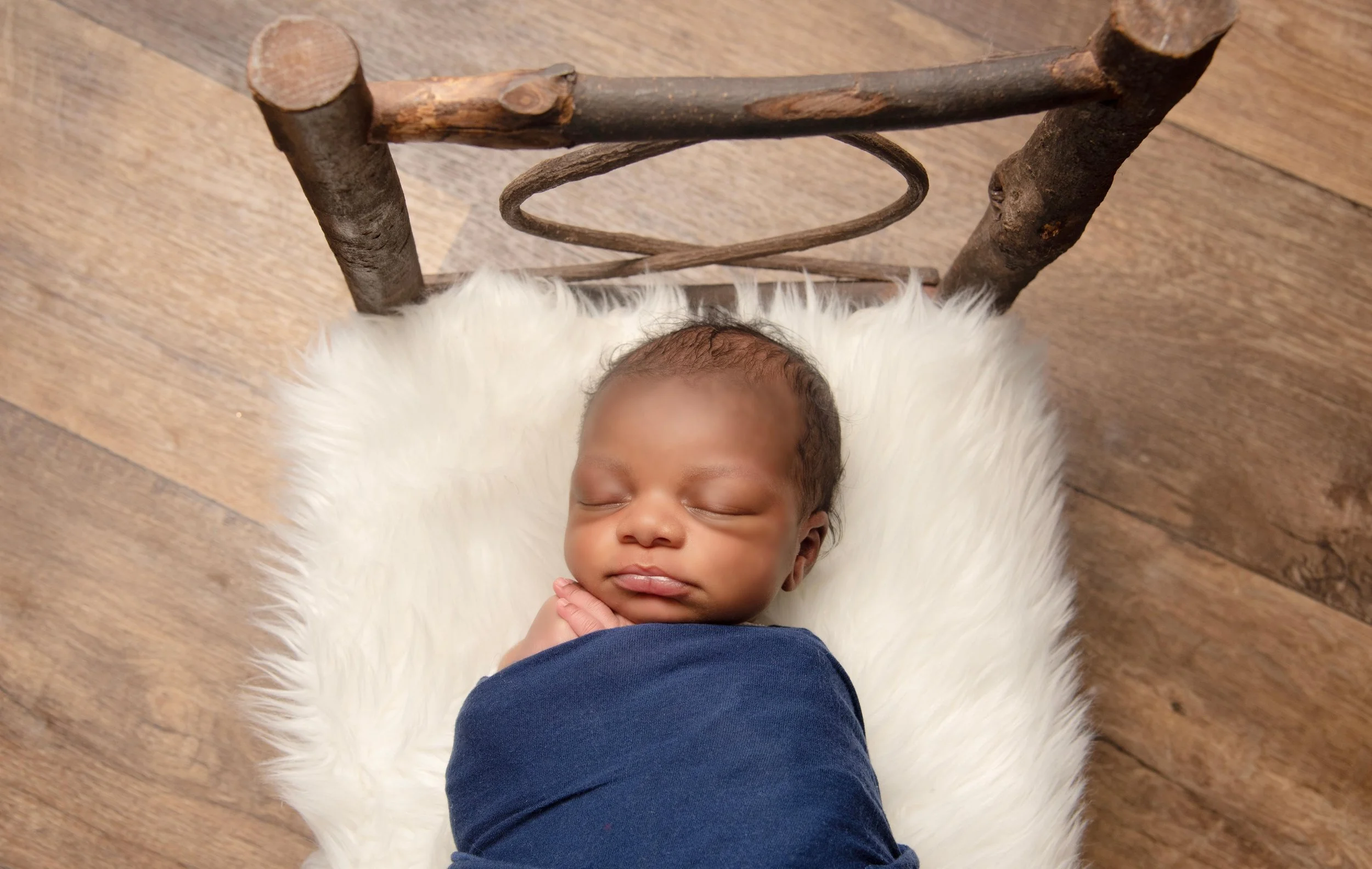 A sleeping baby lying on a white furry blanket on a rustic wooden floor, viewed from above.
