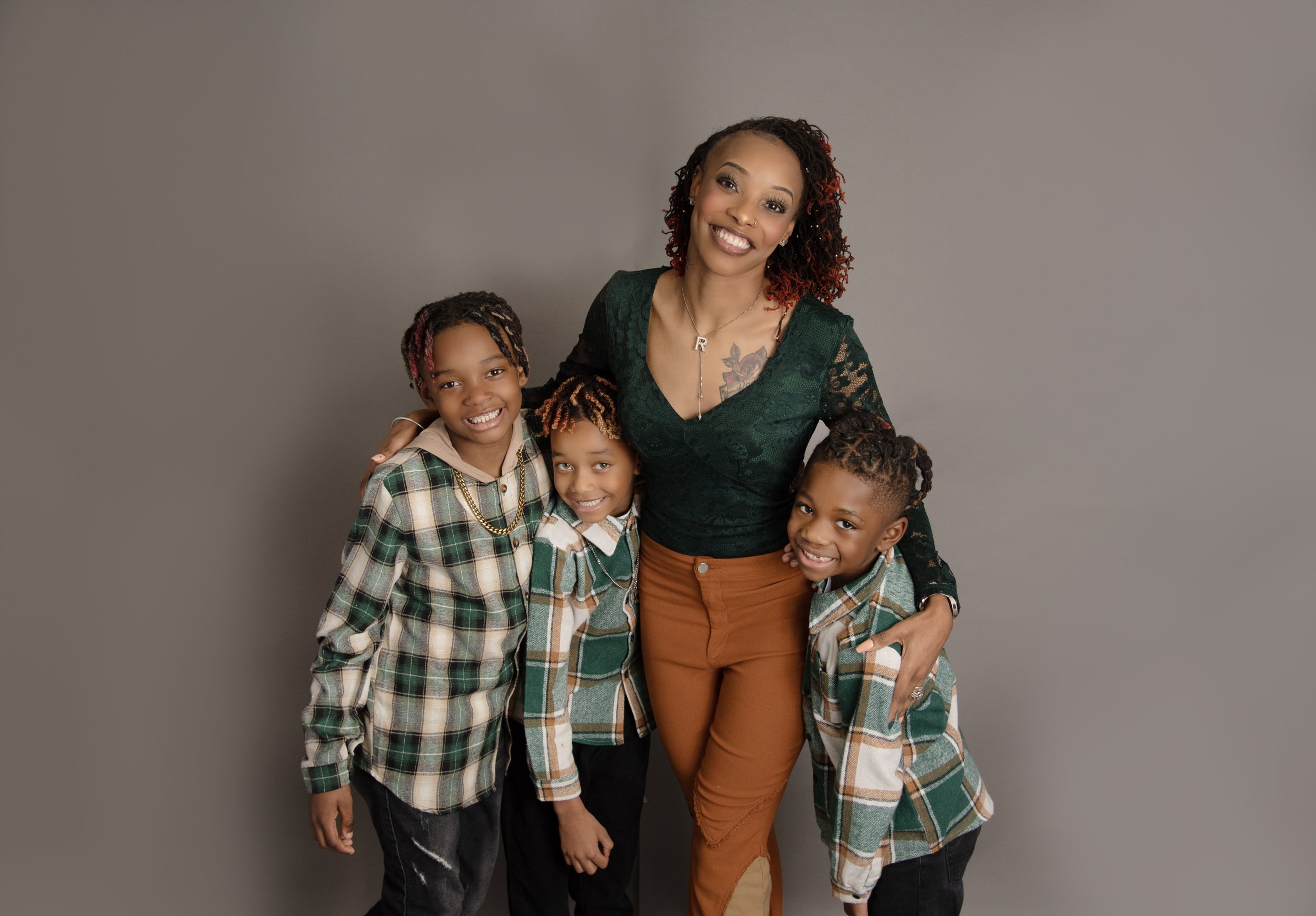 A woman and three children smiling and posing in front of a plain gray background.