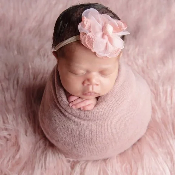 newborn baby girl wrapped in a soft pink sweater wrap in with pink headband on pink furry blanket