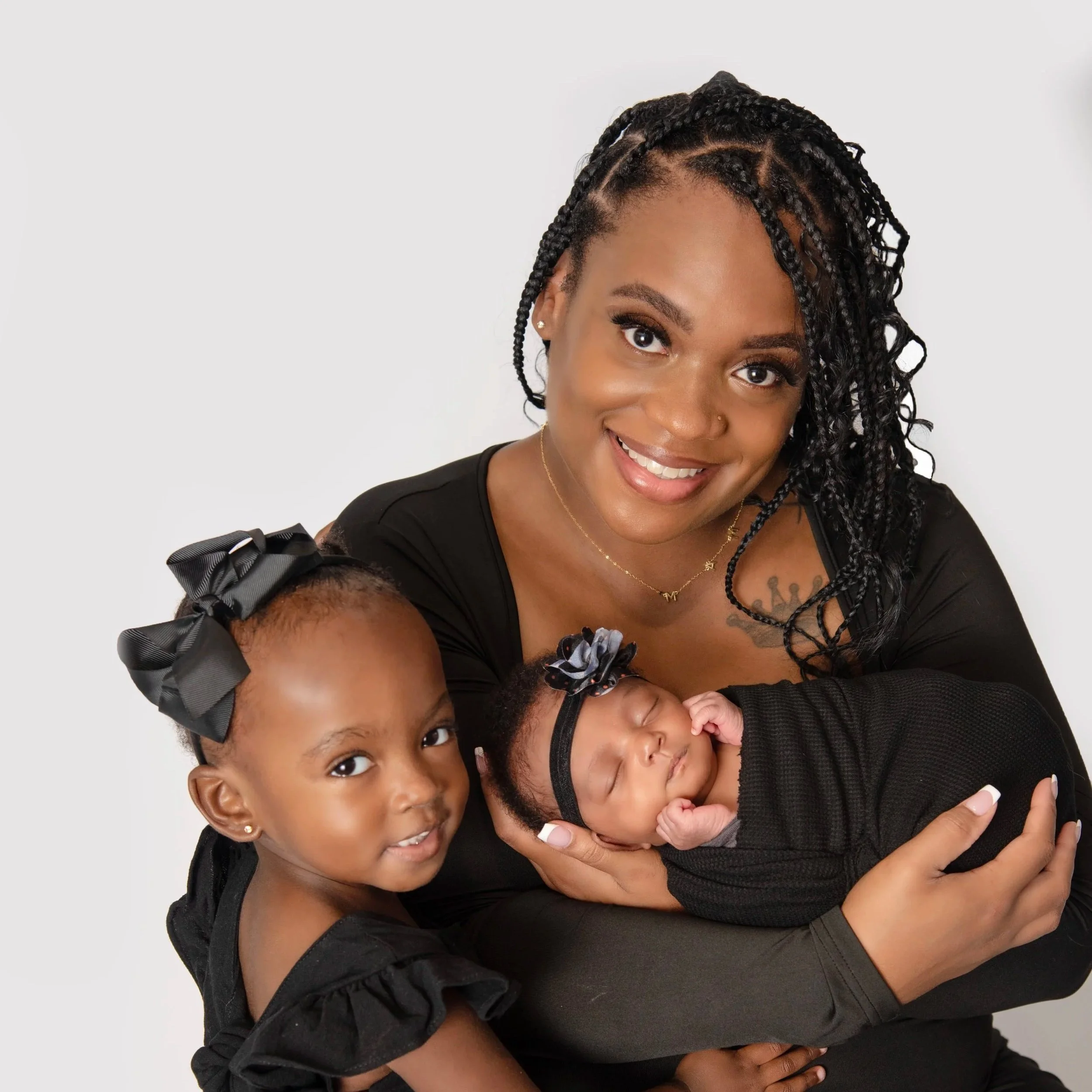 Mom posing with newborn baby girl and toddler daughter wearing black against white backdrop