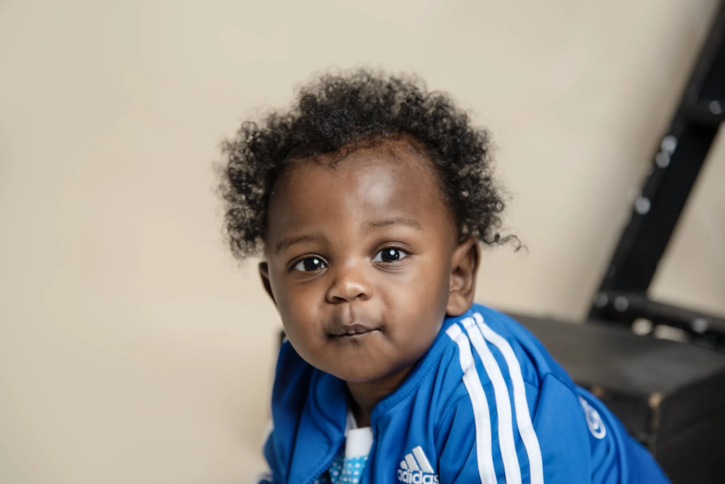 A young child with curly hair wearing a blue Adidas sports jacket.