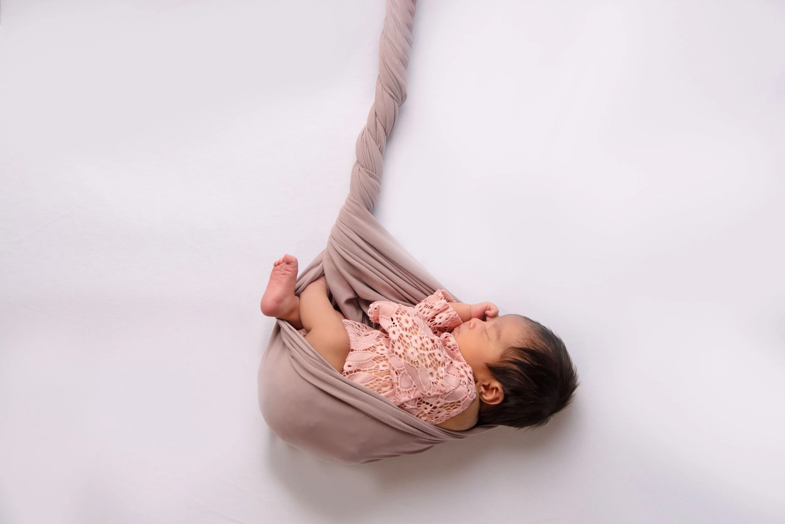 Newborn baby girl in pink lace outfit laying in a mauve colored cocoon