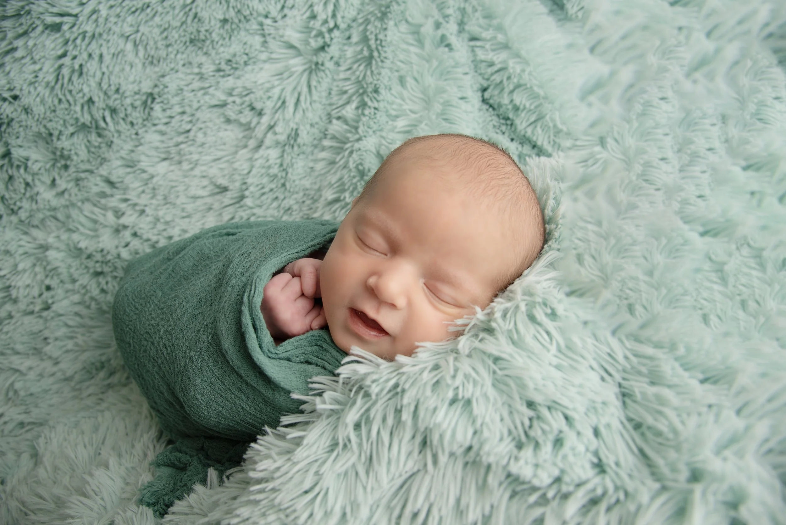 A newborn baby peacefully sleeping on a soft, fluffy mint-green blanket, wrapped in a matching green blanket.
