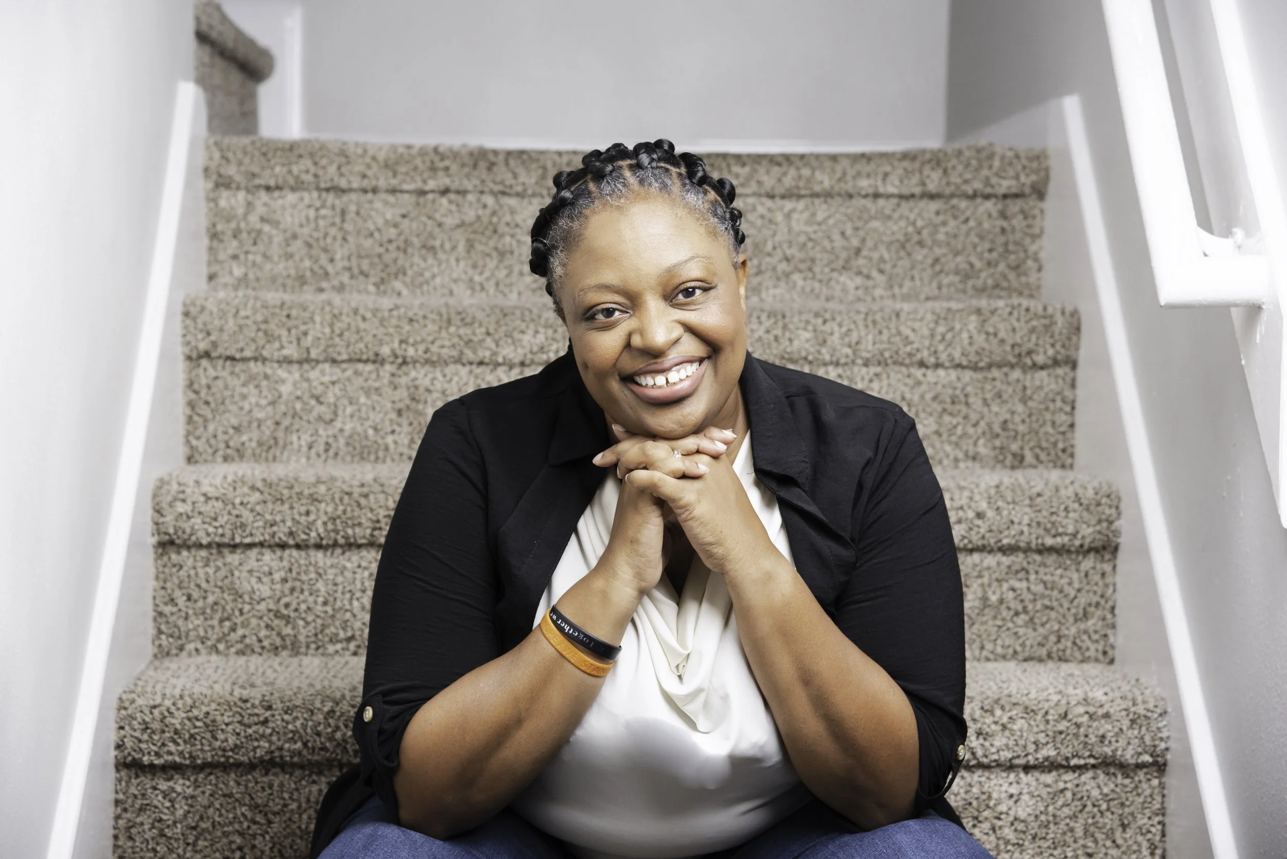 Patricia Johnson, owner of PDJ Photography smiling and sitting on carpeted steps posing for picture.