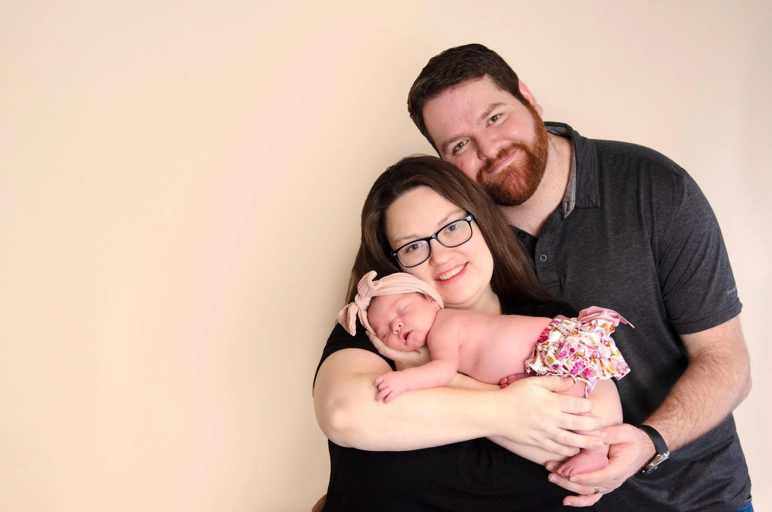 mom and dad standing together and holding newborn baby girl in tutu and headband