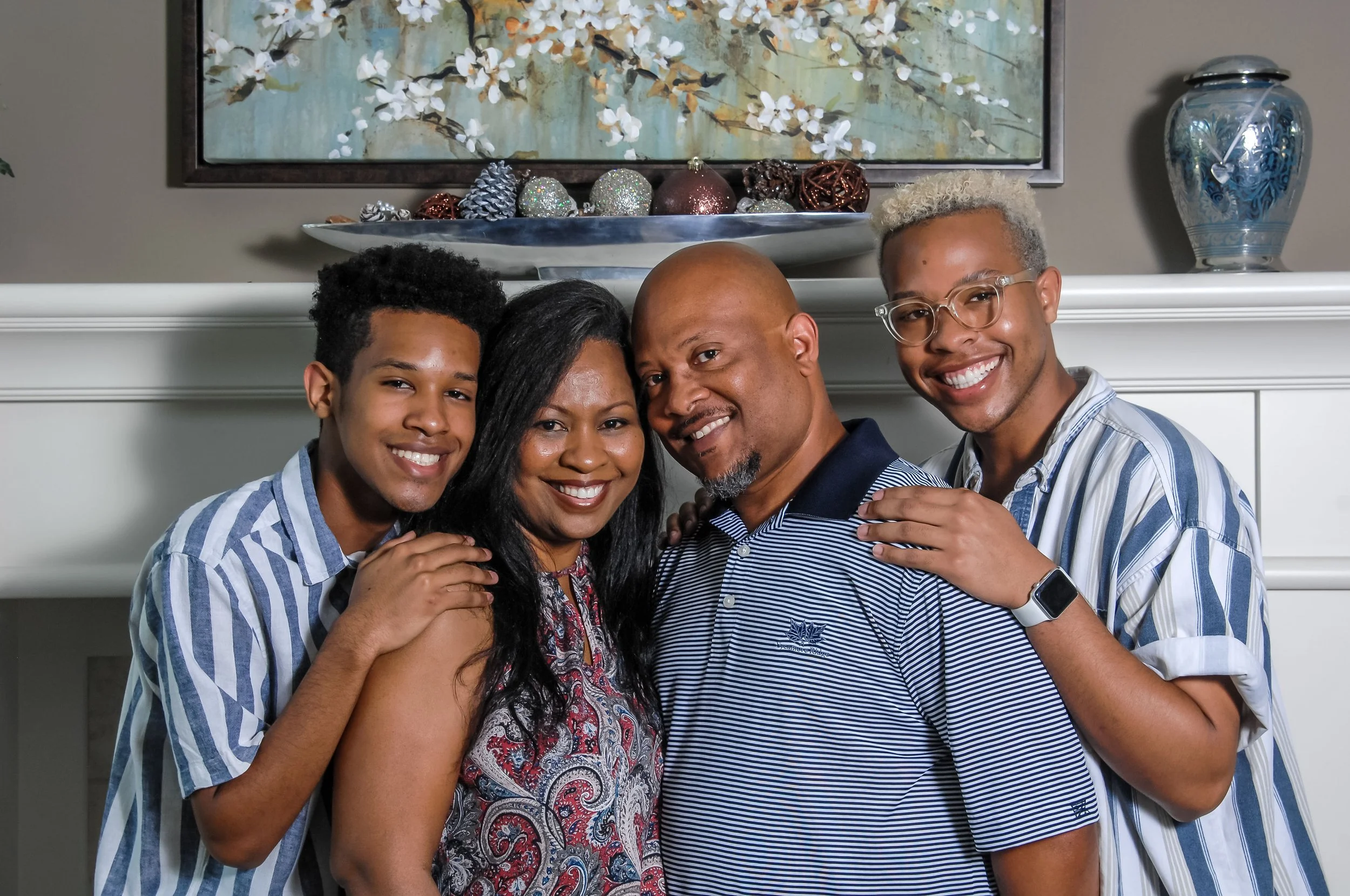 Family of four posing together indoors with a fireplace, holiday decorations, and artwork on the wall behind them.