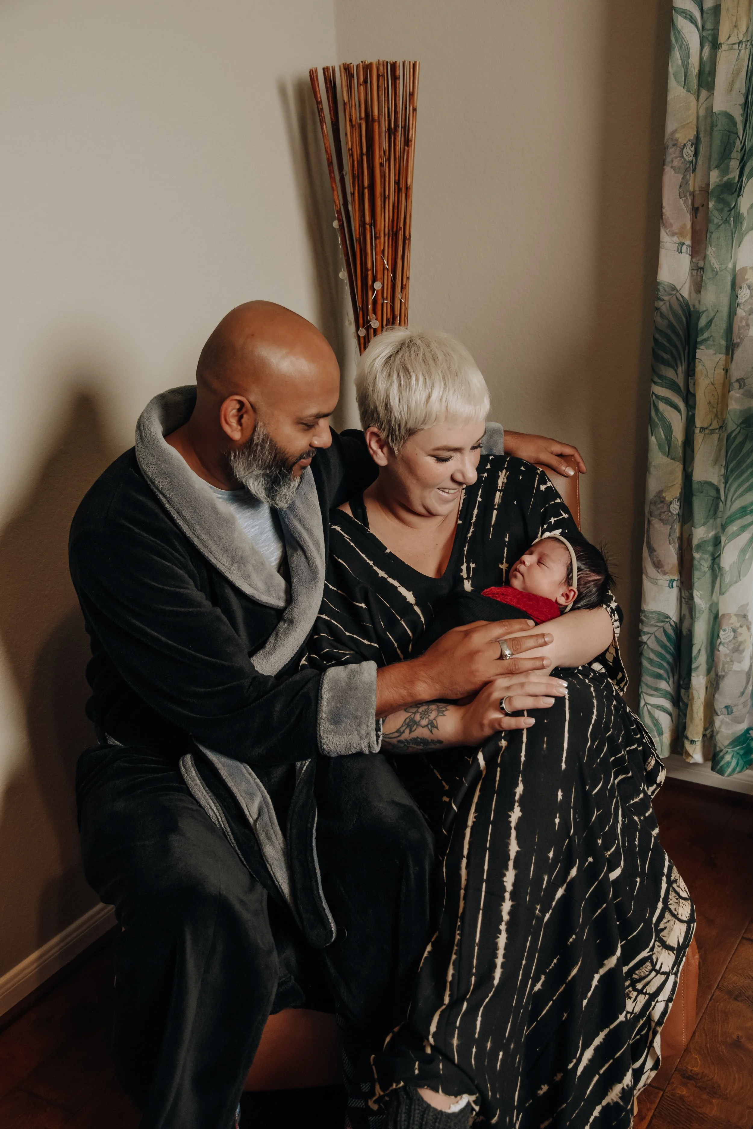 Lifestyle newborn session with mom, dad and baby girl cuddled up in chair in living room