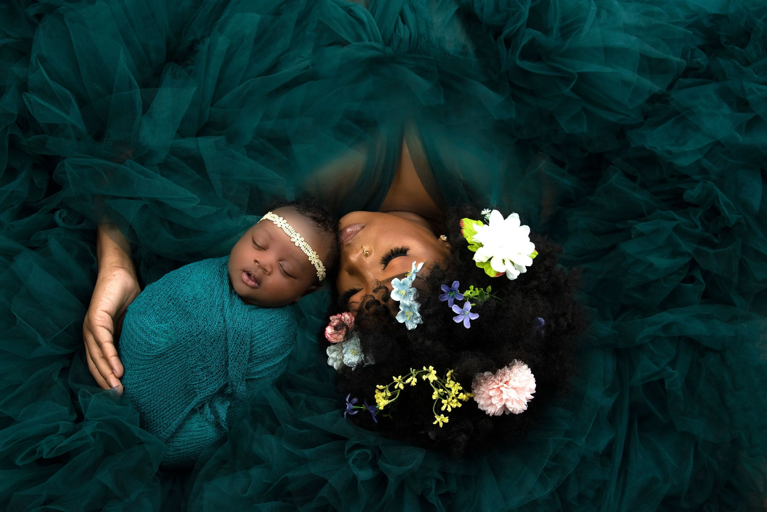 Newborn baby girl wrapped in teal while laying with mom who is in a green maternity robe