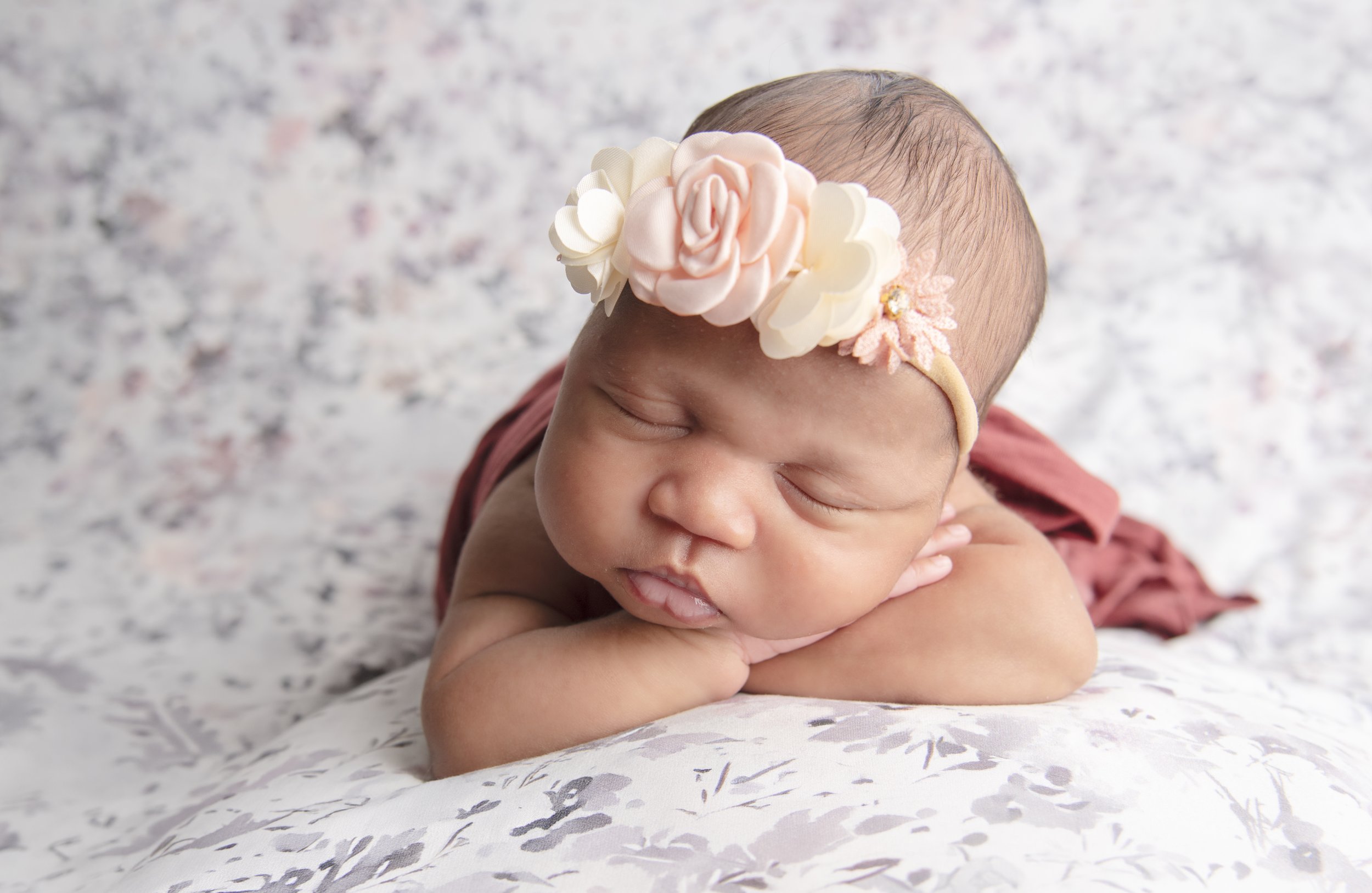 A sleeping baby laying on a floral-patterned blanket, wearing a pink floral headband.
