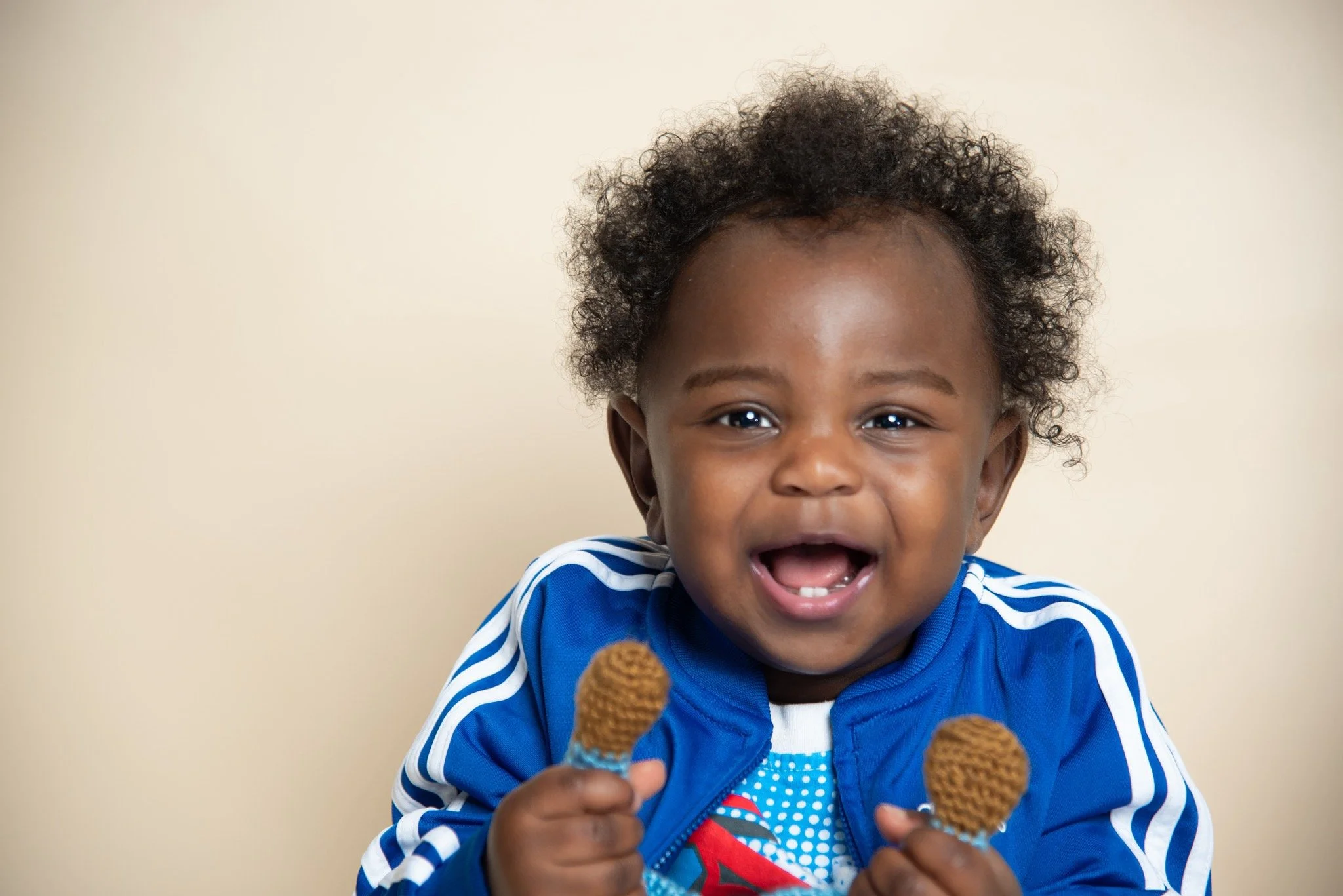 A young child with curly hair, smiling and holding two small ice cream cones against a plain background.