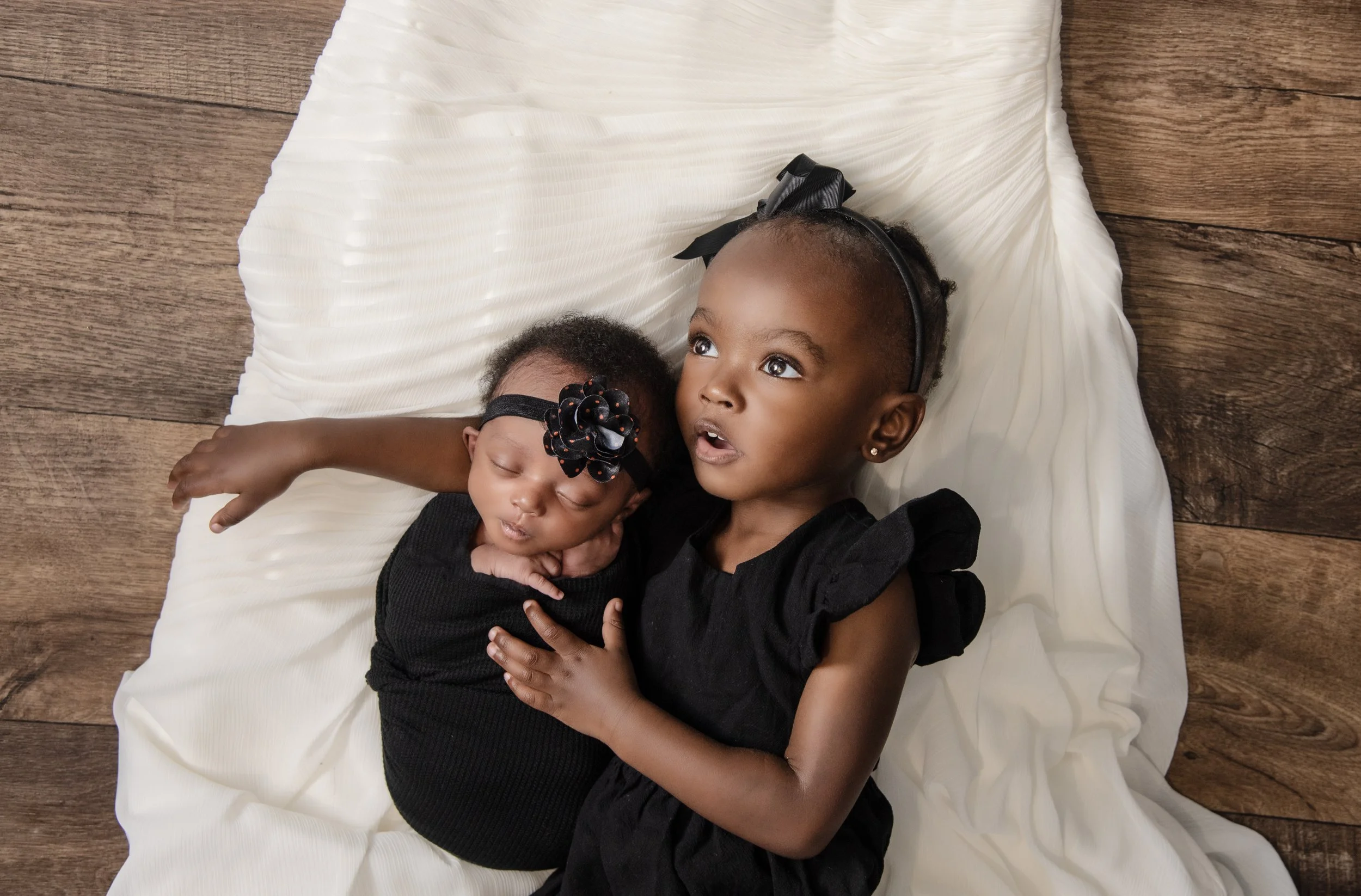Newborn baby girl posed with older sister laying on mom's wedding dress