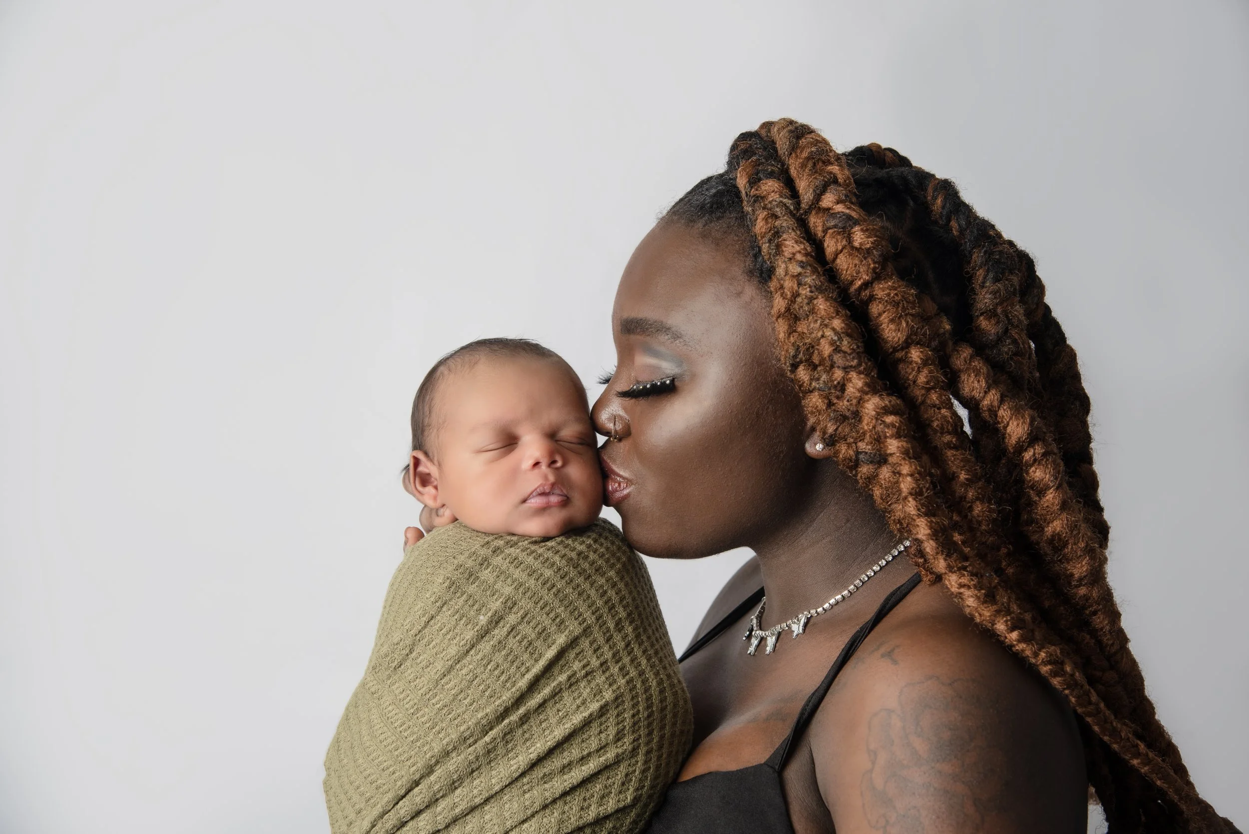Newborn baby boy wrapped in sage fabric being kissed by mom in studio