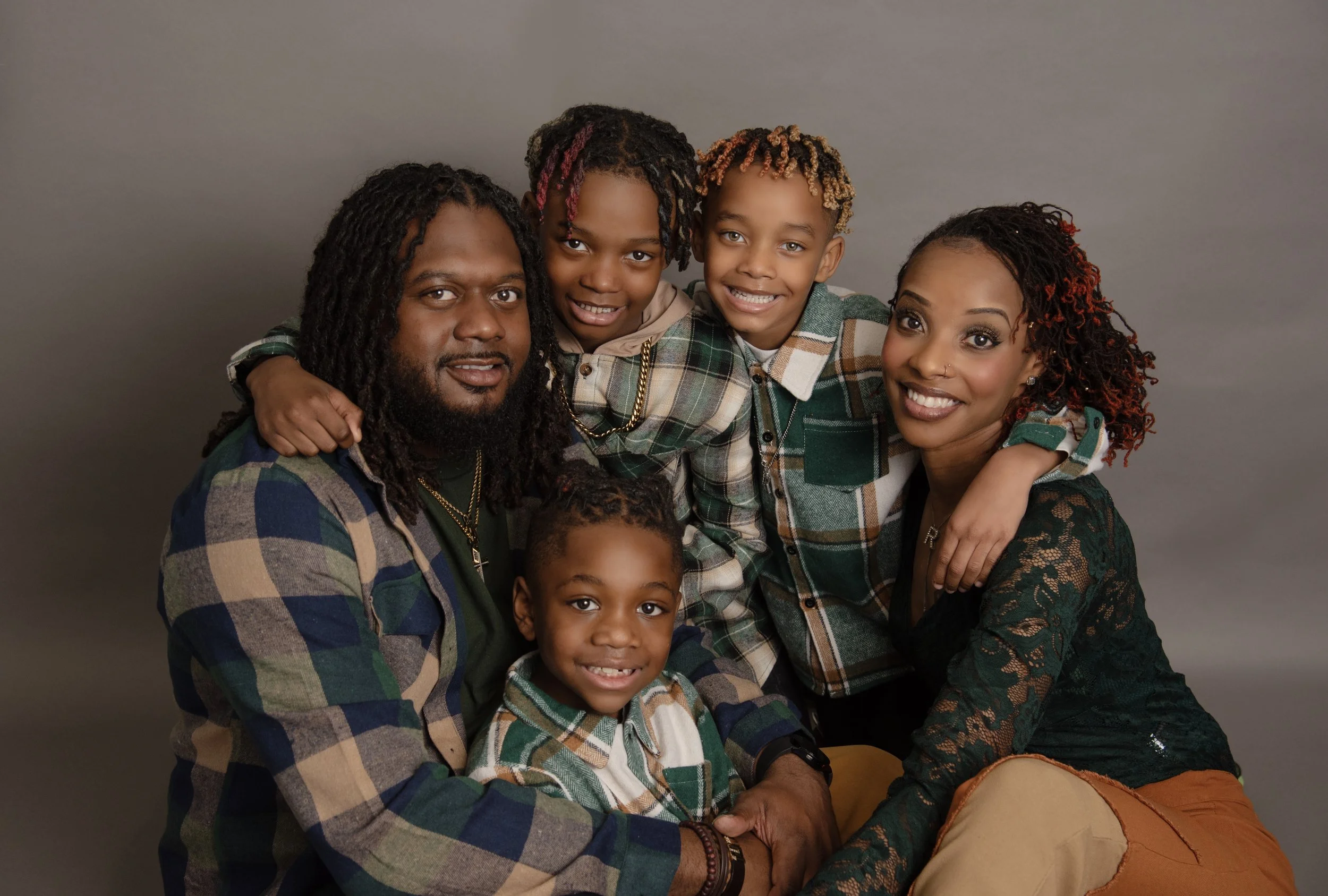 A family of six posing together, all wearing casual plaid clothing, with a neutral gray background.