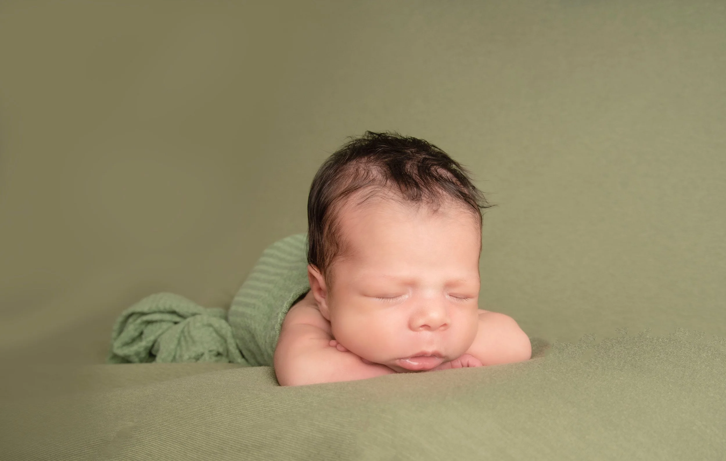 Newborn baby girl wrapped in sage color fabric against olive green fabric background