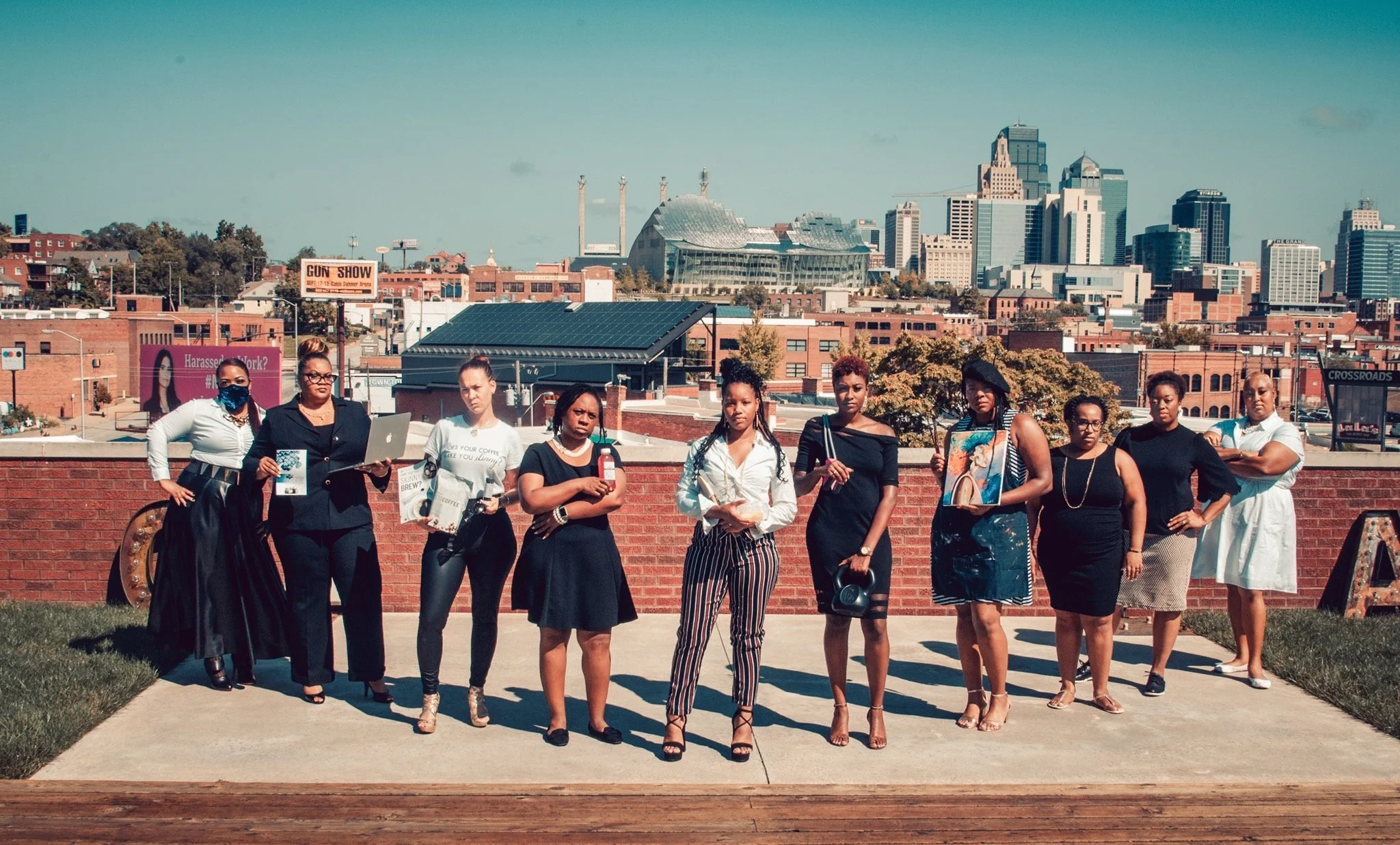 A group of ten women standing on a rooftop with an urban city skyline in the background. Some women are holding books or bottles, and one is wearing a mask for women entrepreneurs branding session.