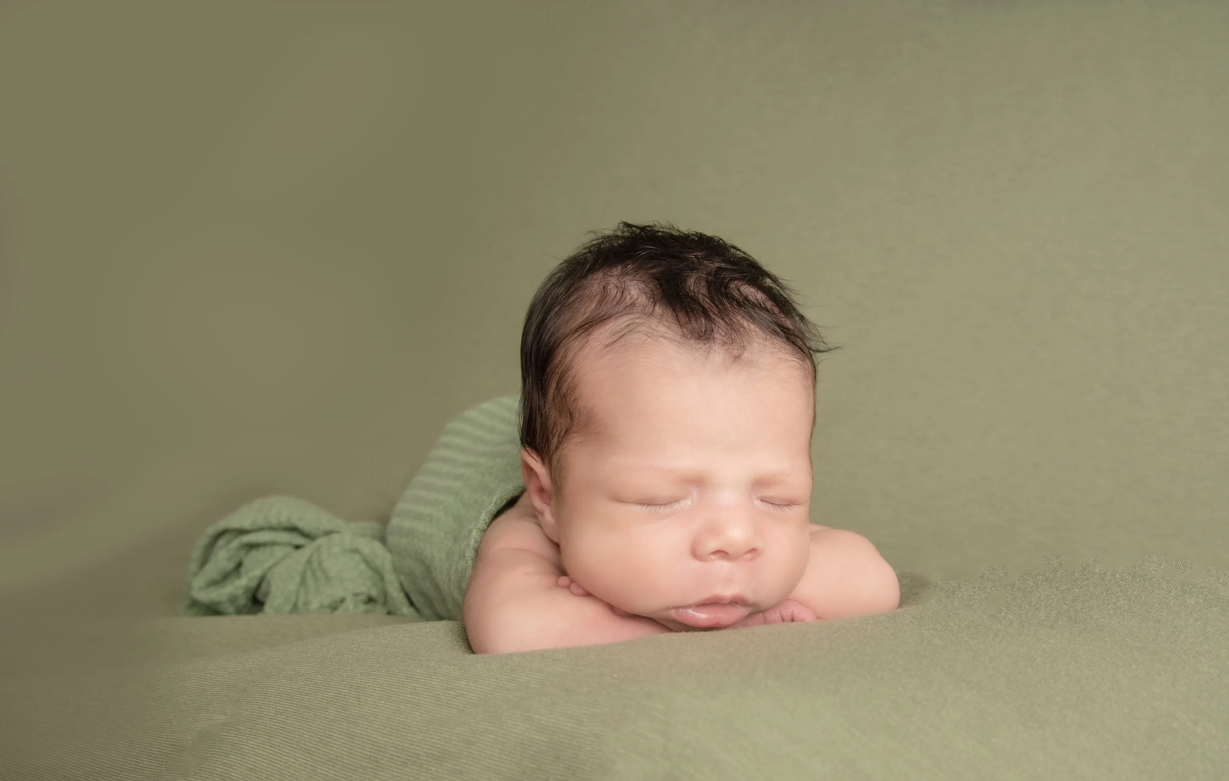 A sleeping baby lying on a green surface with their head resting on their arms.
