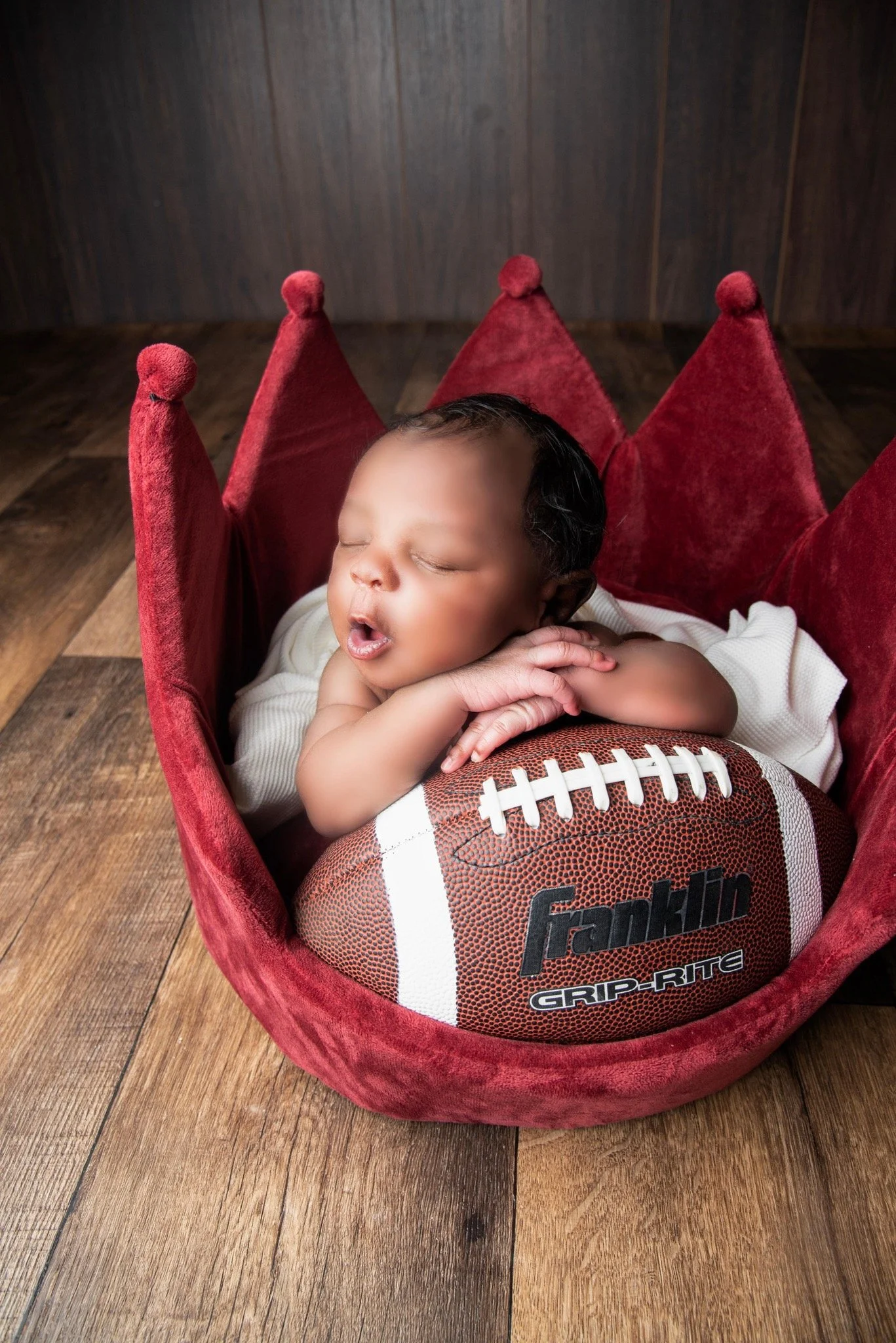 Newborn baby boy in crown prop propped against football