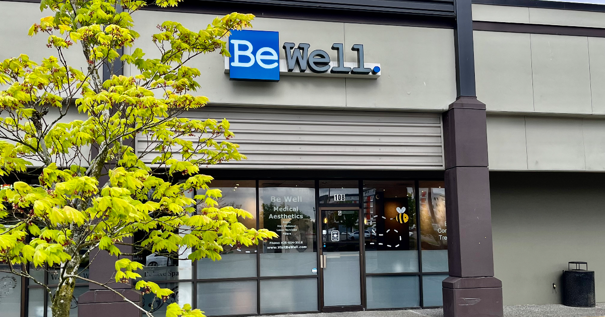 Storefront with sign for Be Well Medical Aesthetics, located in a strip mall. There is a tree with bright green leaves in front of the store.