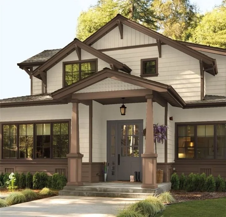 Front view of a two-story white house with brown trim, entry porch with columns, and a front door with glass panels, surrounded by green lawn and trees.