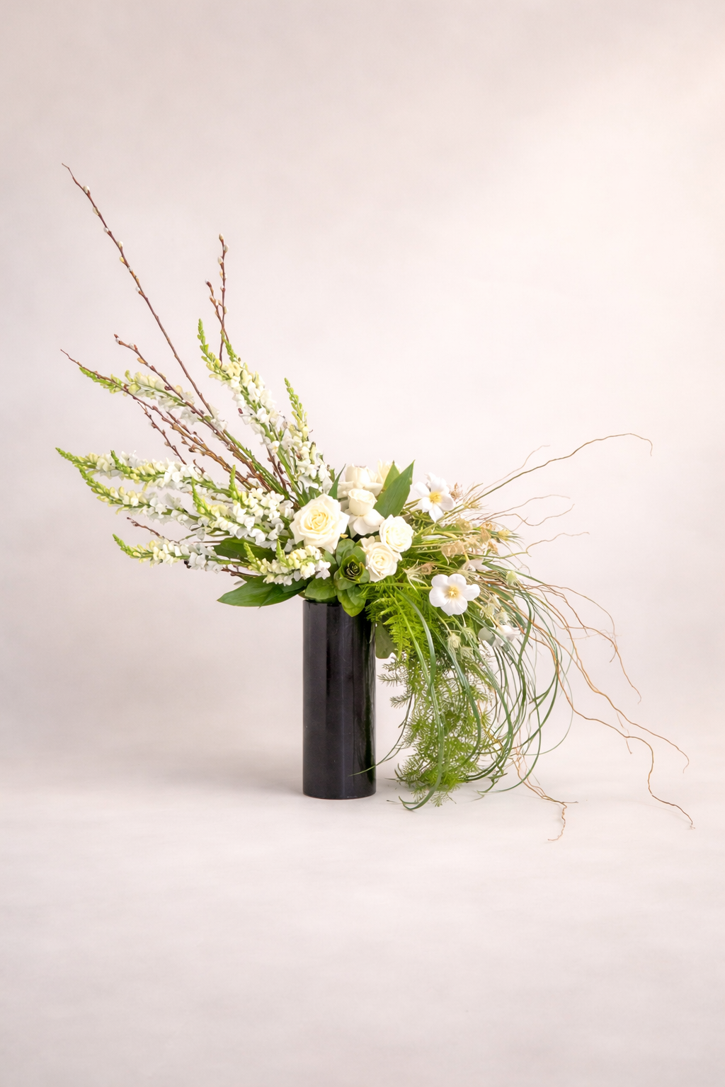 Elegant white floral arrangement with roses, tulips, and greenery in a tall, black vase.