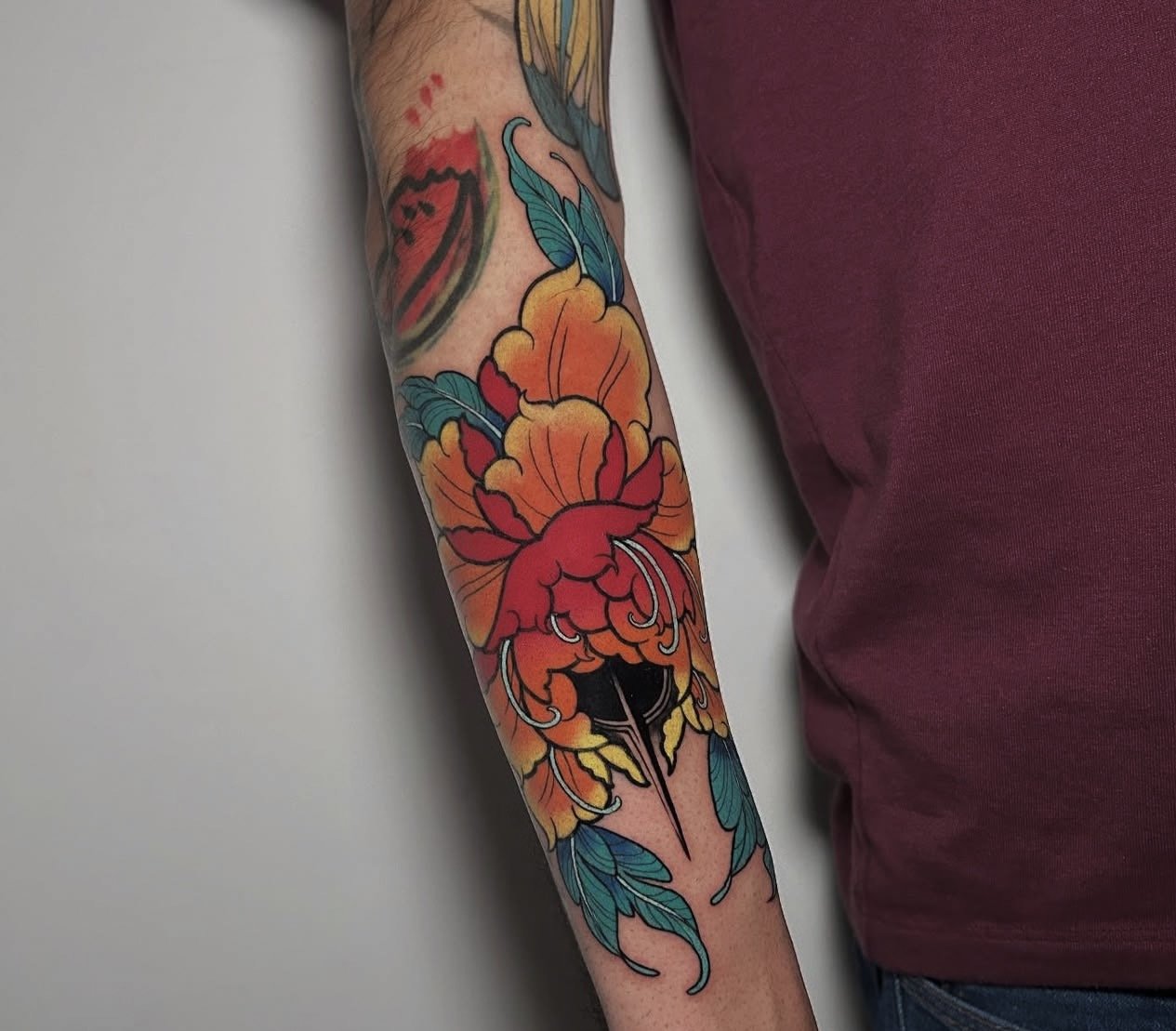 Colorful tattoo on a person's arm featuring a large orange and red flower with green leaves.