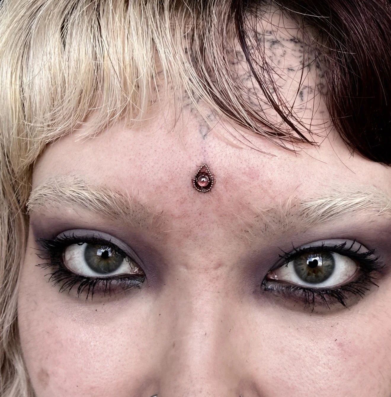 Close-up of a person's face, focusing on their eyes, eyebrows, and forehead, with a decorative gemstone forehead piercing.