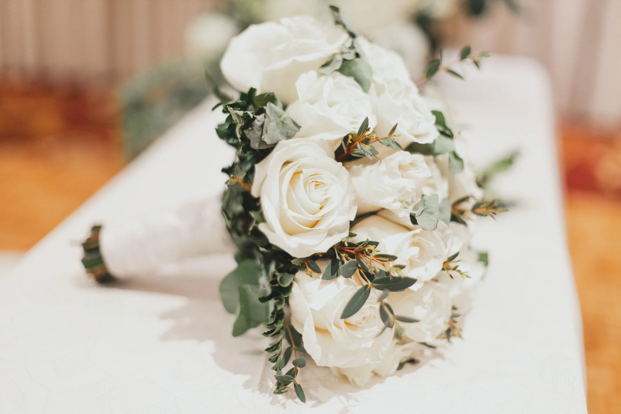 Ramo de flores blancas, principalmente rosas con hojas verdes, sobre una mesa blanca
