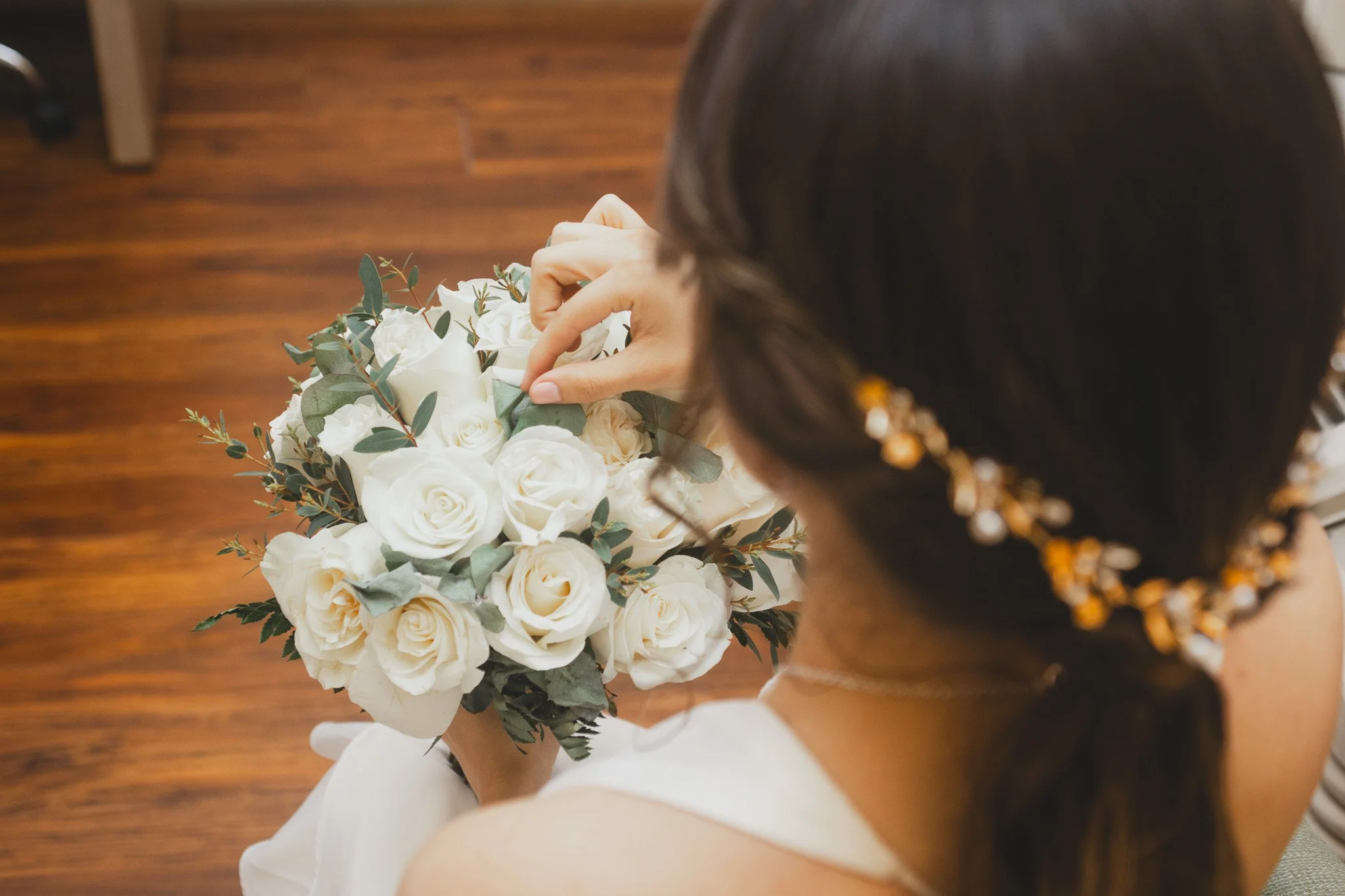 Mujer sosteniendo ramo de rosas blancas y follaje en una habitación con piso de madera.