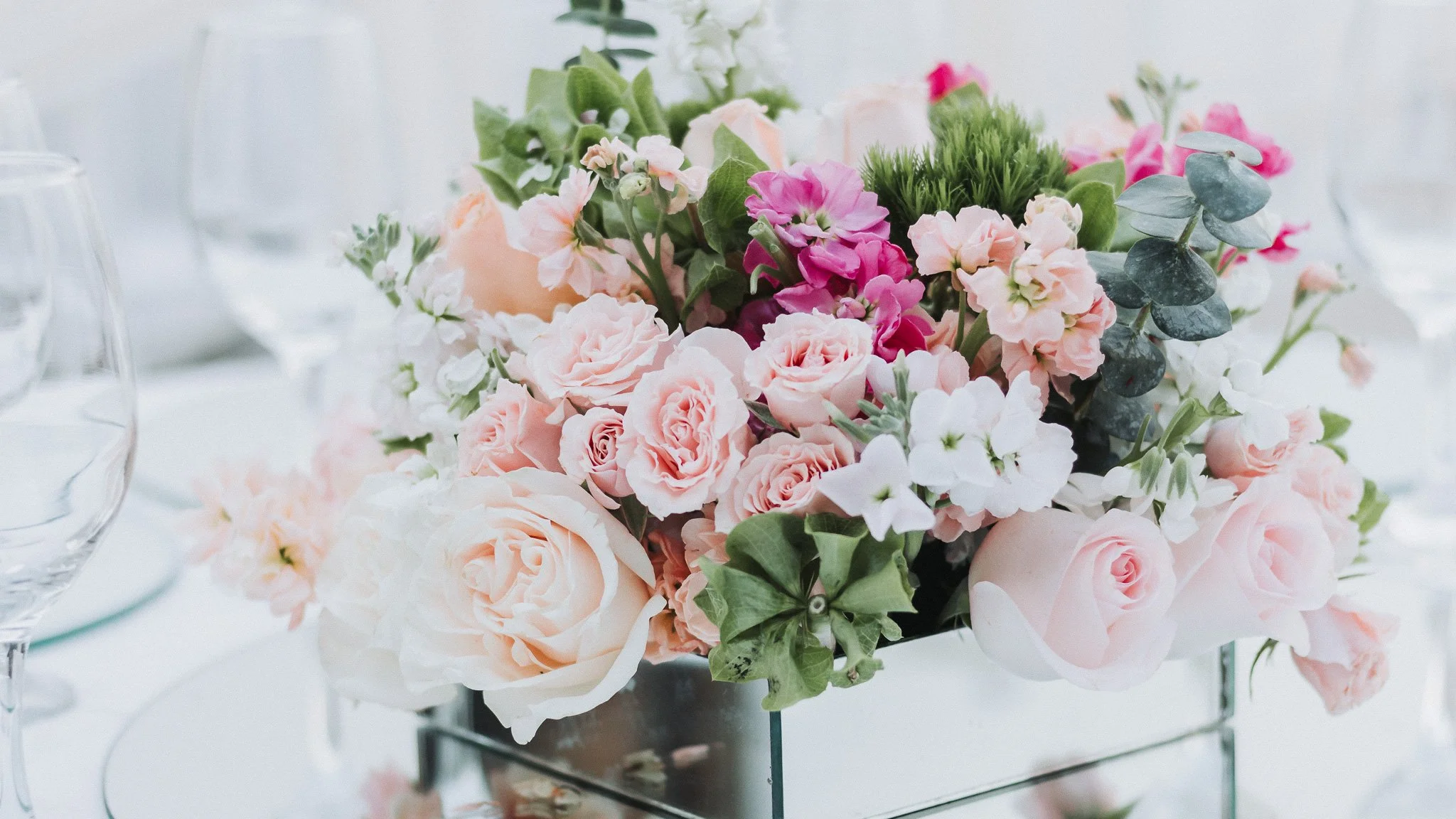 Ramo de flores variadas en tonos rosados y verdes en una mesa elegantemente decorada.