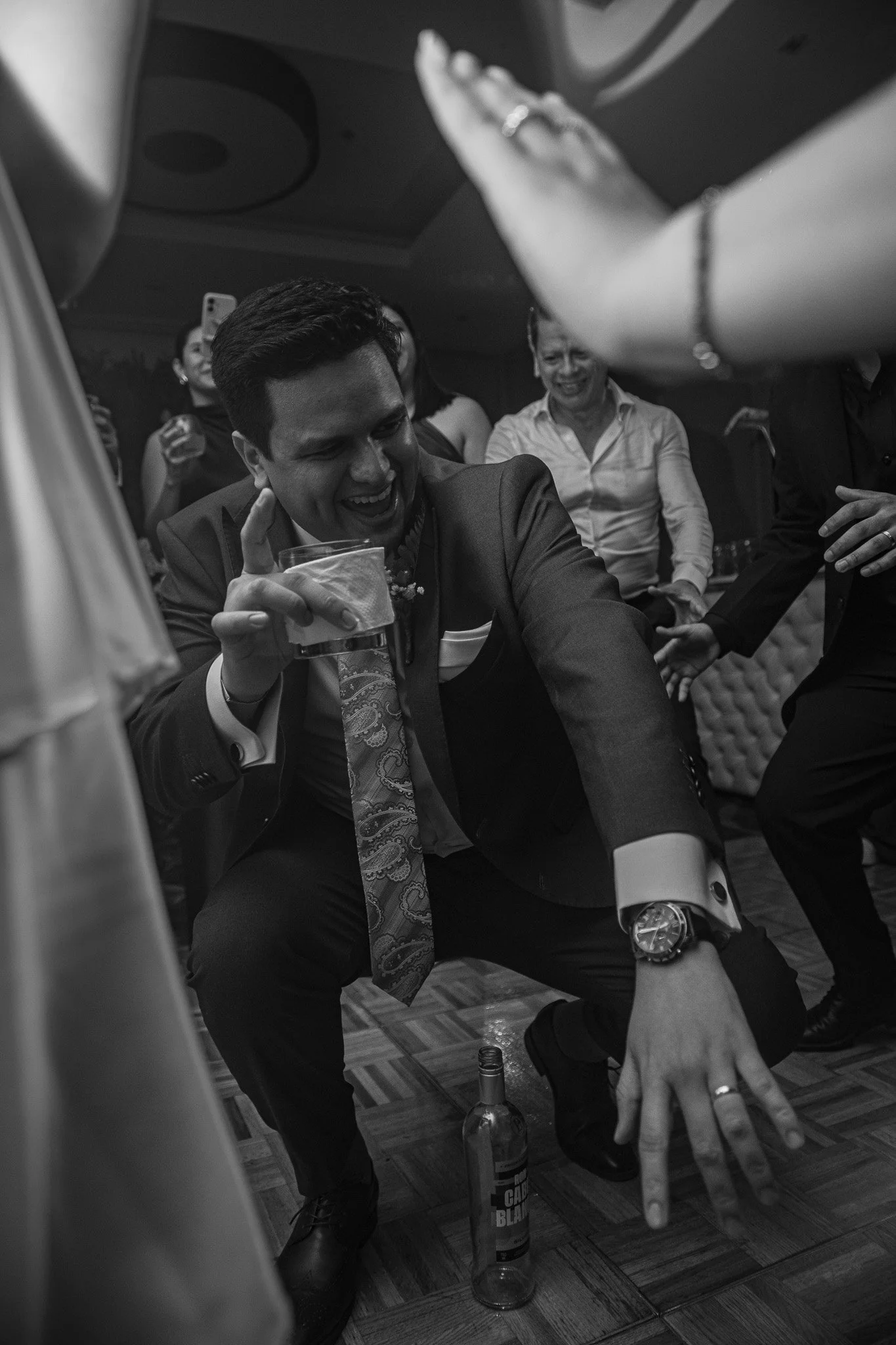 Grupo de personas felices en una fiesta, con un hombre en traje de novio en el centro, sosteniendo un vaso y bailando, rodeado de amigos en la pista.