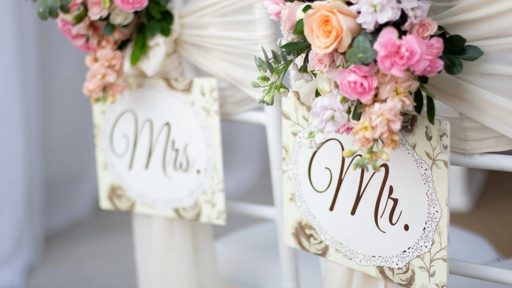 Carteles con las palabras 'Mrs.' y 'Mr.' en un escenario decorado con flores en tonos rosa y durazno para una boda.
