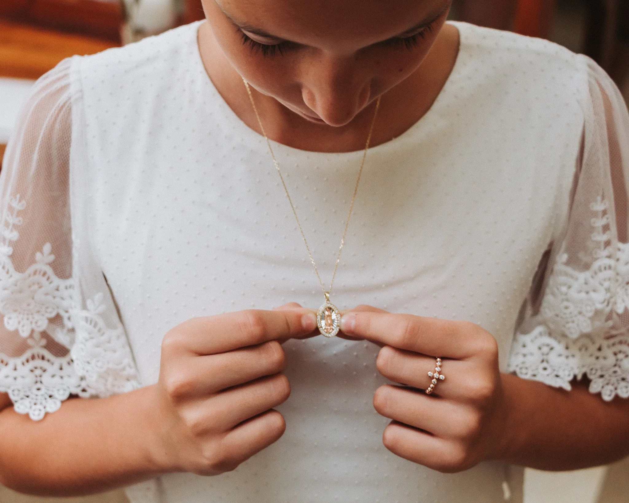 Mujer con blusa blanca de manga de encaje sosteniendo un collar con un dije en forma de óvalo