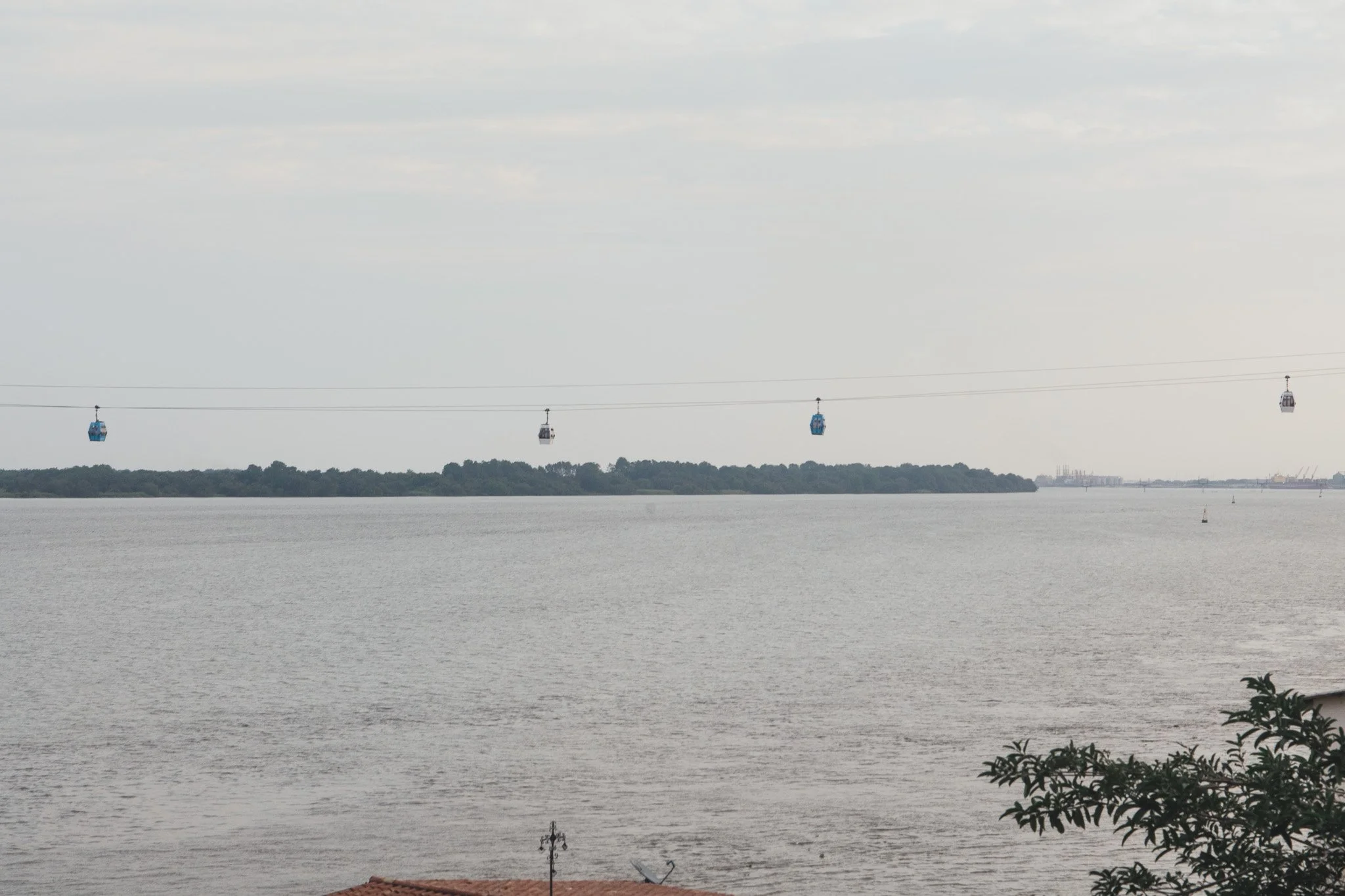 Vista panorámica de un río con teleférico en el cielo y vegetación en primer plano.