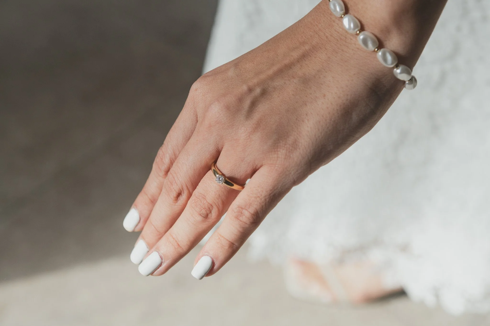 Mano con anillo de matrimonio y pulsera de perlas blancas