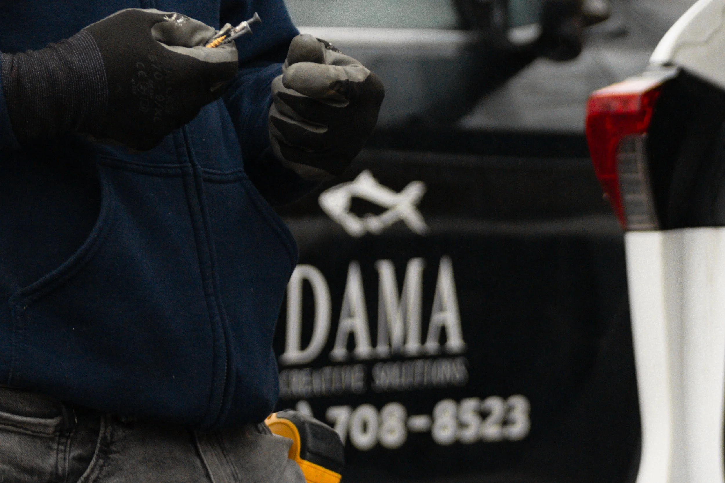 Person wearing black gloves holding a small object in front of a black vehicle with white text on it.