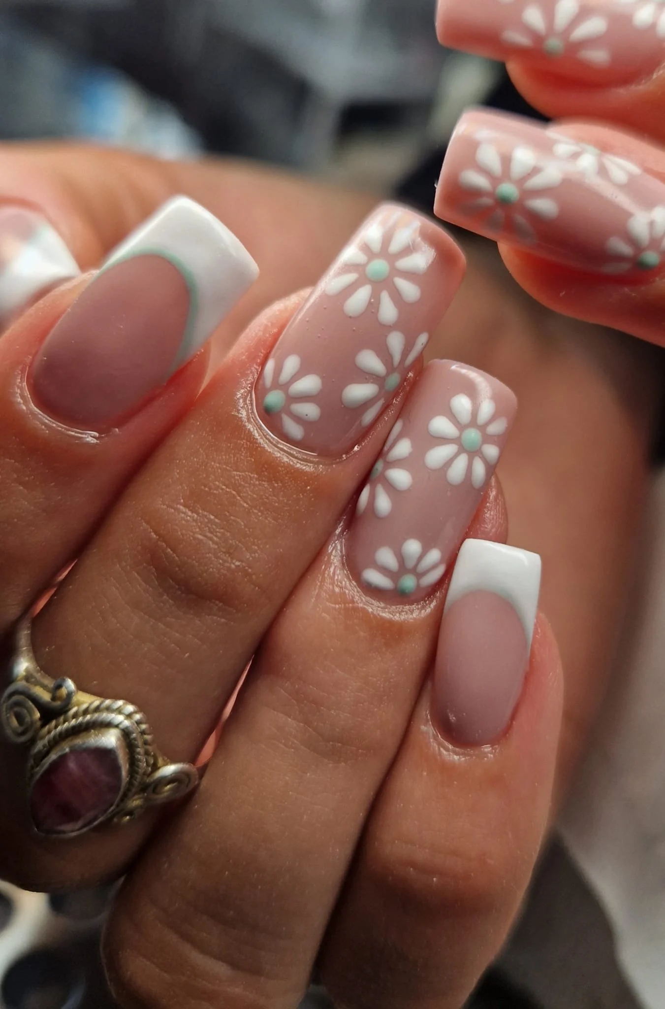 Close-up of manicured fingernails with pink and white floral nail art, including some nails with white tips.