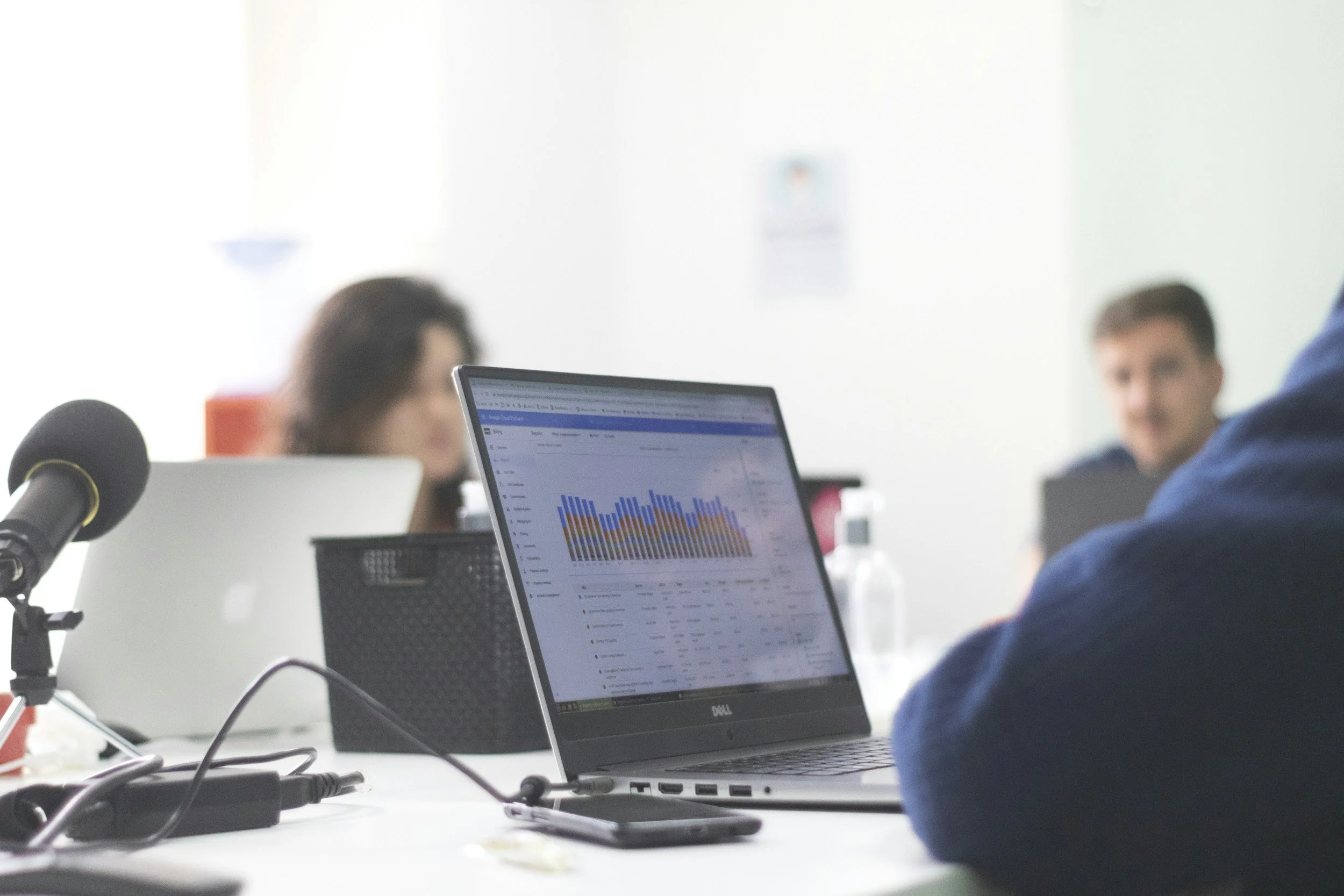 Business meeting with people working on laptops, one displaying a graph on a screen, in a modern conference room.