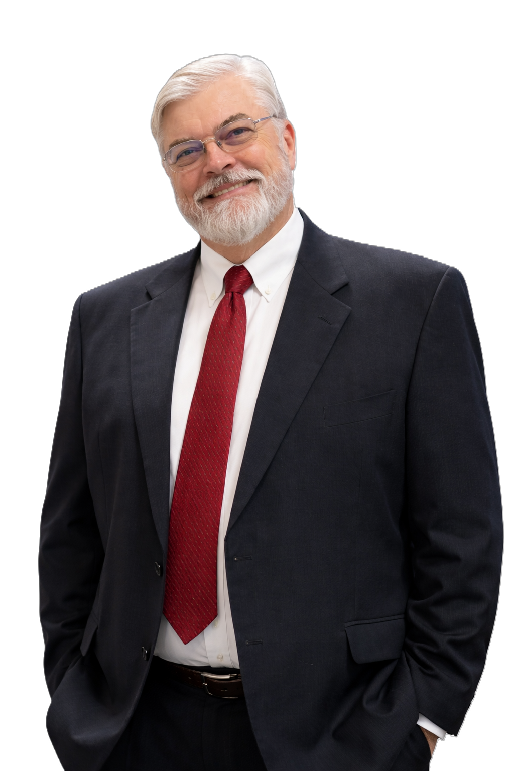 A smiling elderly man with white hair and a beard, wearing glasses, a dark suit, a white shirt, and a red tie, standing with one hand in his pocket against a black background.