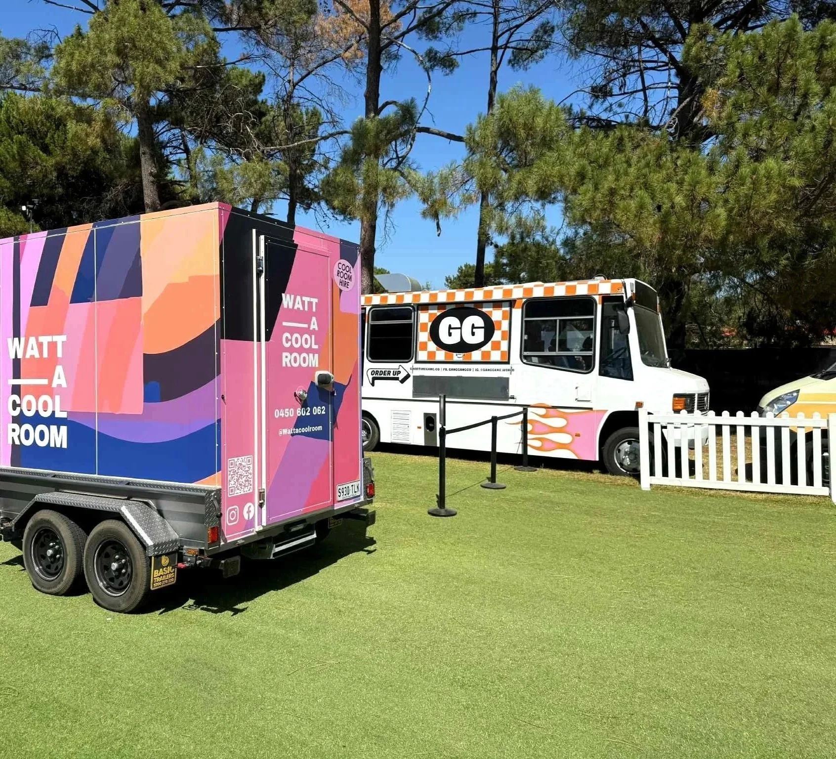 Pink, black, and orange decorated truck with slogan 'Watt a Cool Room' parked on grass with trees in background.
