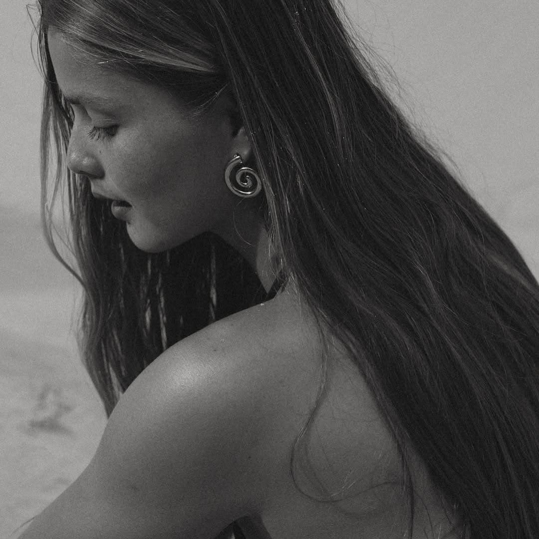 Black and white photo of a woman with long hair looking down, wearing a spiral earring.