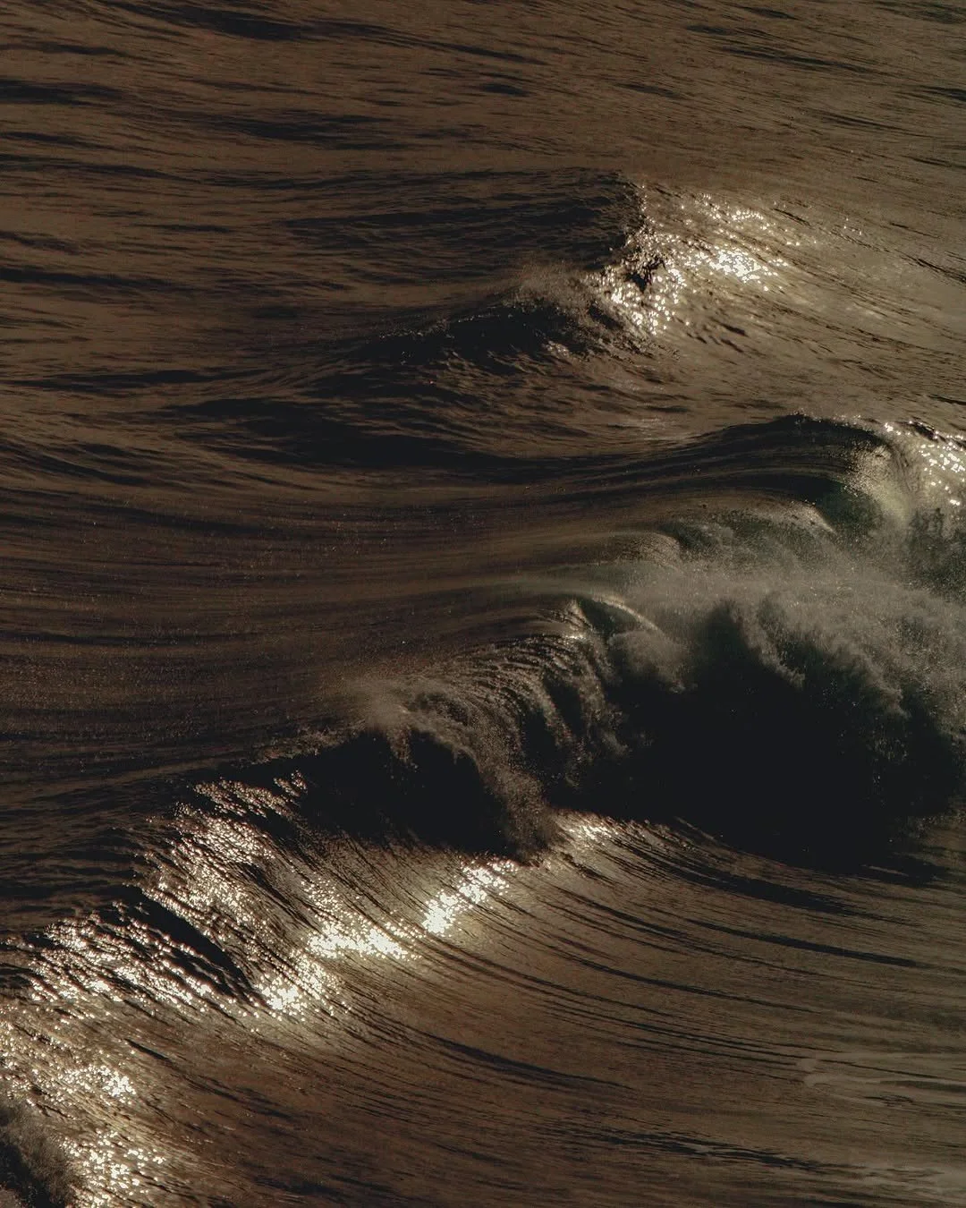 Close-up of ocean waves with sunlight reflecting off the water at sunset or sunrise.