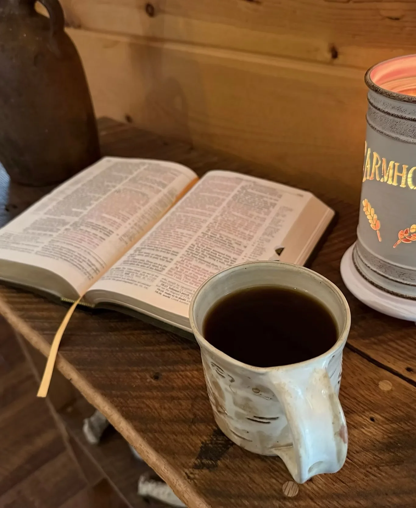 Open book, ceramic mug filled with black coffee, and a decorative candle on a wooden table.