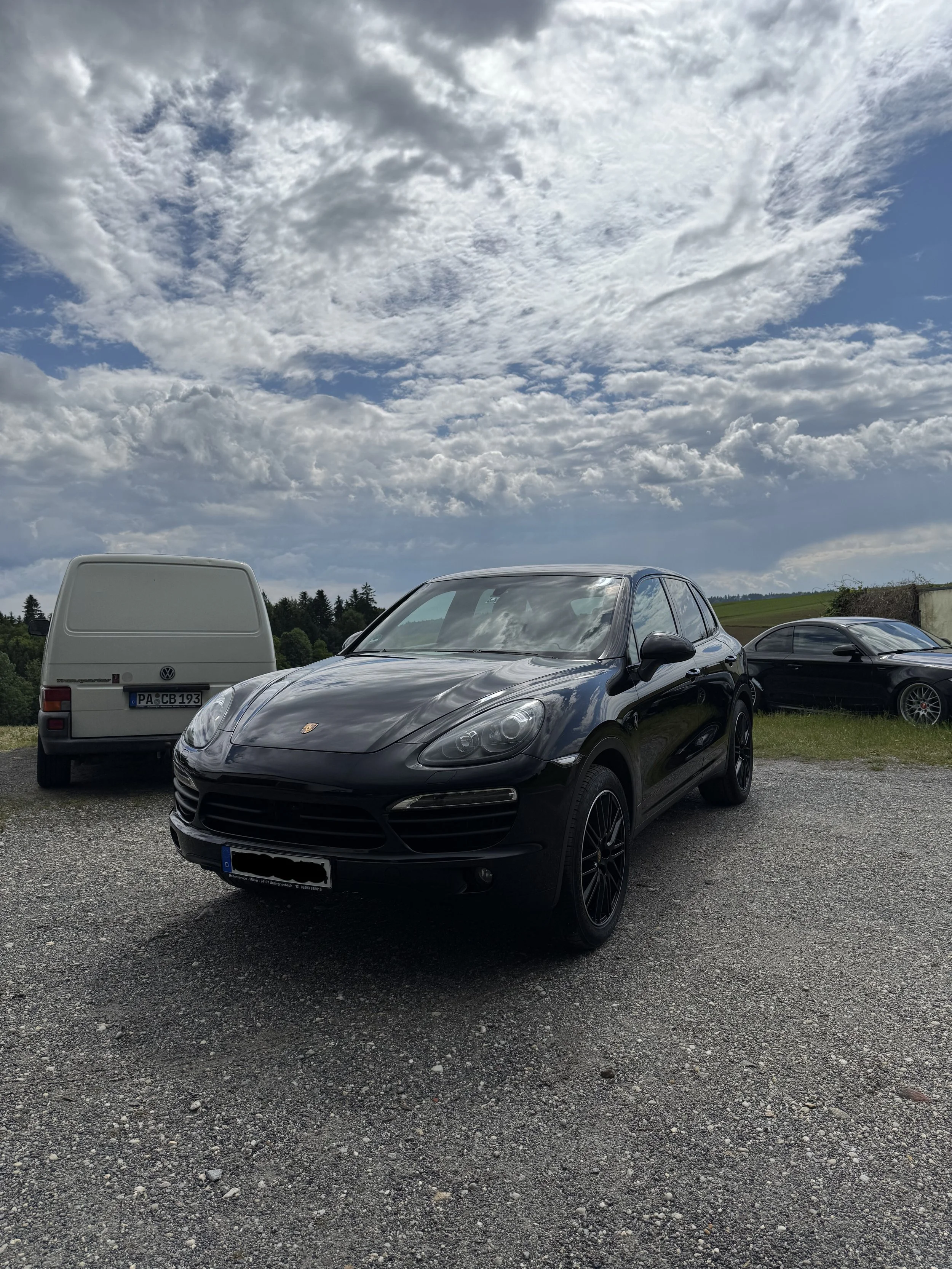 Schwarzer Porsche SUV parkt auf einem Parkplatz mit vier weiteren Fahrzeugen darunter eine weiße VW Transporter und ein schwarzer Sportwagen Autoaufbereitung in Passau. Keramikversiegelung Hutthurm