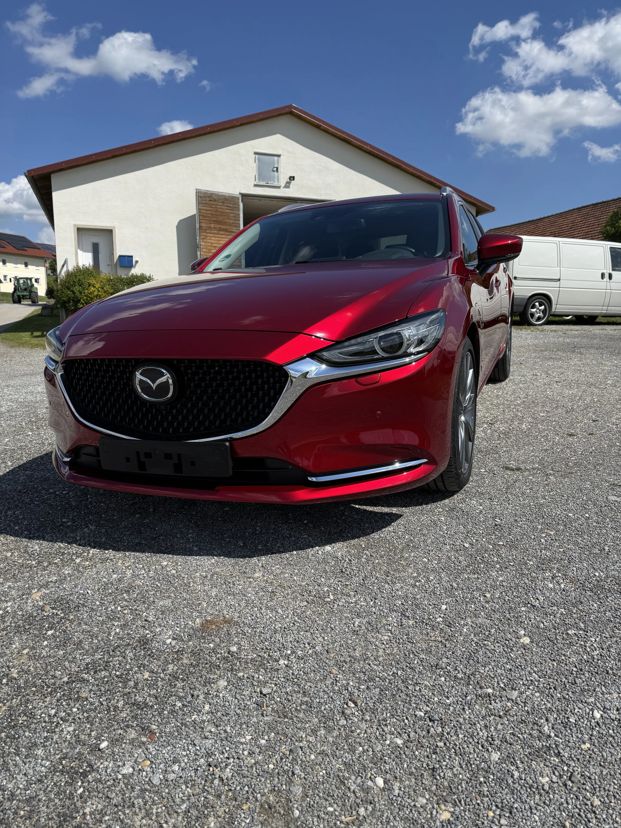Roter Mazda-Auto vor einem weißen Haus auf einem gepflasterten Bereich bei sonnigem Himmel.Keramikversiegelung Passau. Professionelle Autoaufbereitung Passau Hutthurm