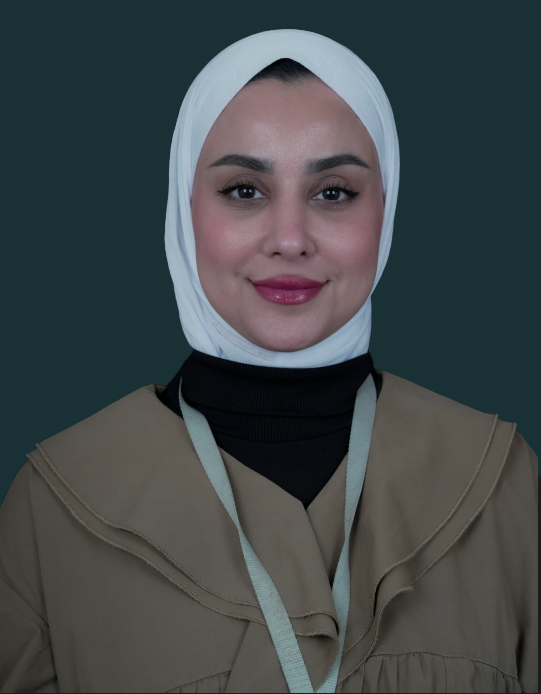 A young woman wearing a white hijab, black turtleneck, and beige jacket smiling against a dark background.