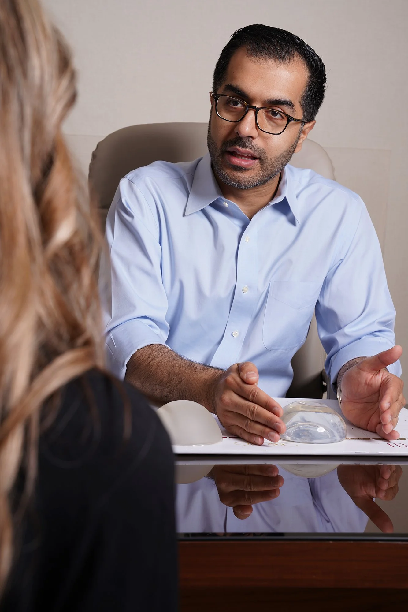 Husain AlQattan sits at a table during a consultation, talking to a woman with long hair, with a glass animal model on the table.