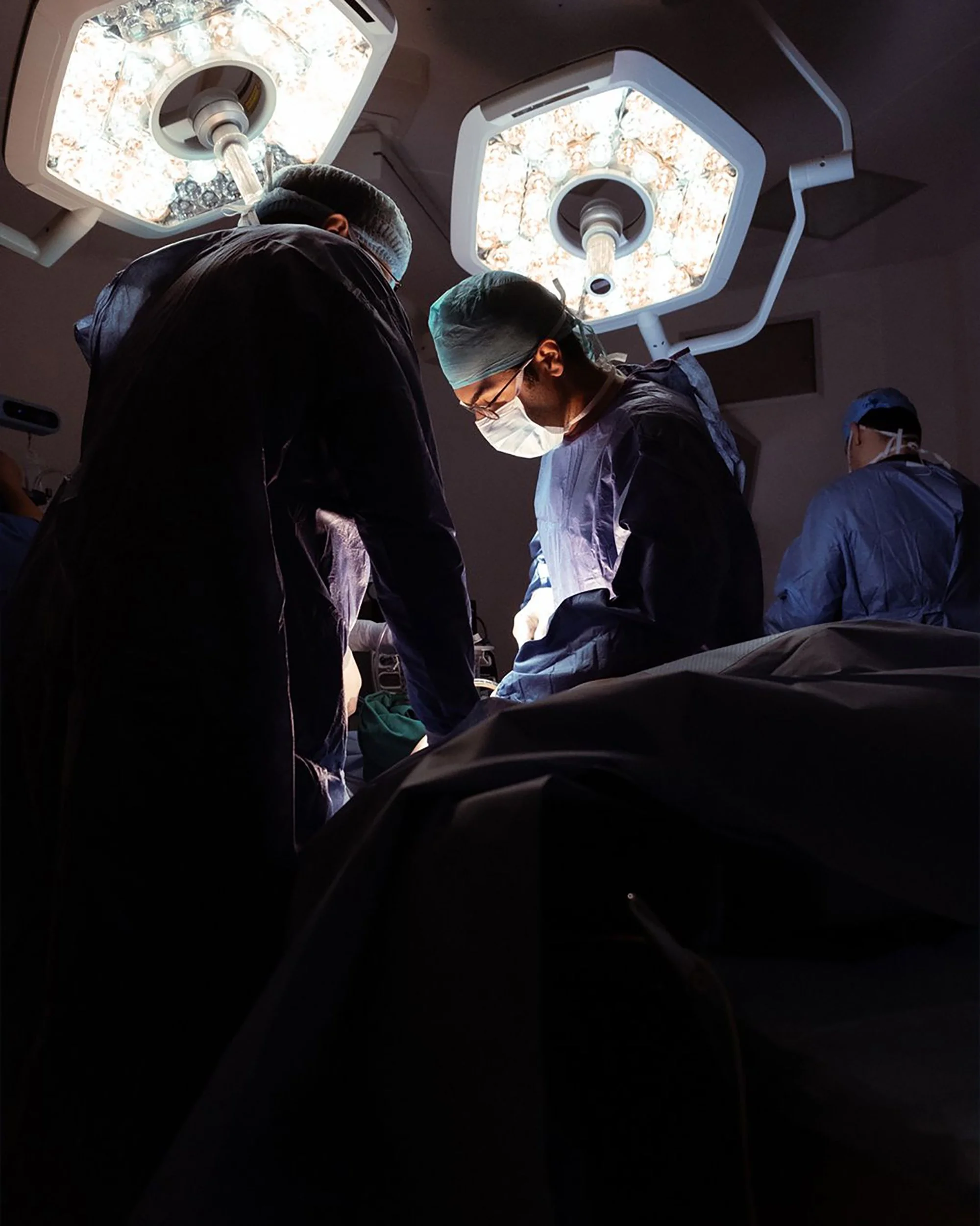 Husain AlQattan. Medical professionals performing surgery in an operating room with bright overhead lights.